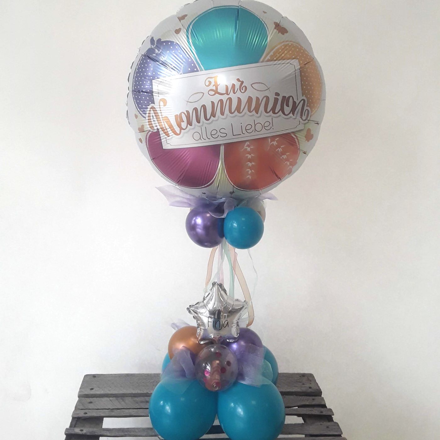 Tischbouquet mit großem bunten Folienballon 'Zur Kommunion – alles Liebe!' mit lila, türkisfarbenen und goldenen Latexballons, Dekoband, Sternballon und Konfetti-Ballons