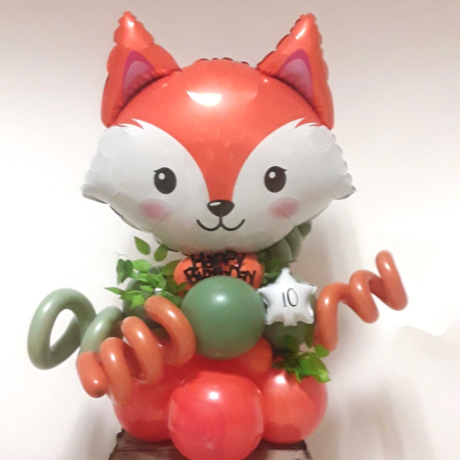Ballonfigur mit großem Fuchs-Folienballon in Orange und Weiß, grüne Pflanzenoptik und orangene und grüne Spiralballons, weißer Sternballon mit Aufdruck '10', Happy-Birthday-Schriftzug in schwarz.