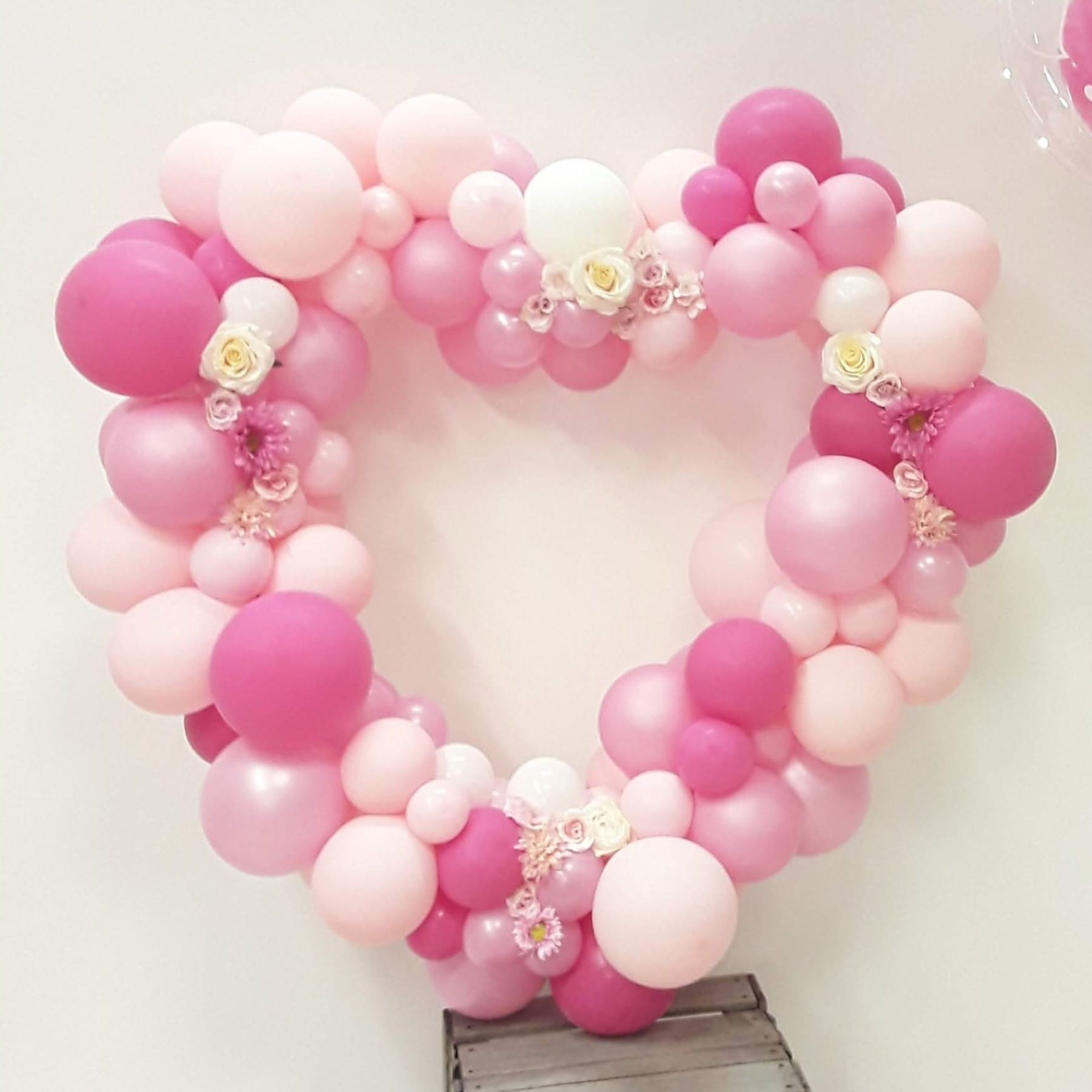 Herzförmiger Ballonbogen in verschiedenen Rosatönen, dekoriert mit weißen und rosafarbenen Kunstblumen