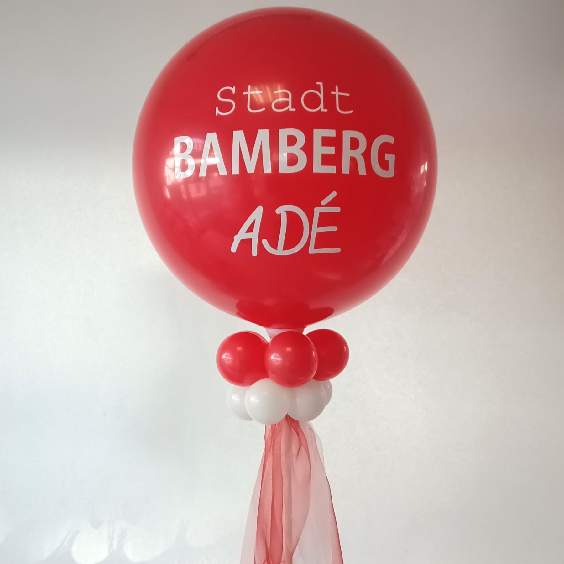 Großer roter Ballon mit weißem Aufdruck 'Stadt Bamberg Adé', dekoriert mit weißen und roten Ballons am Ständer und rotem Chiffonband.