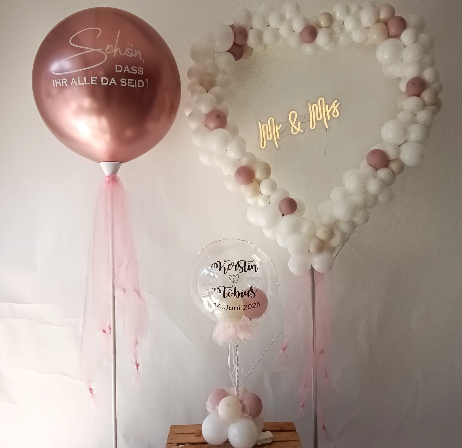 Herzförmige Ballondekoration aus Luftballons in verschiedenen Farben, gefüllt mit kleinen und großen Ballons, teilweise mit Metallic-Effekt, dekoriert auf einem Gestell, mittig mit Schriftzug „Mr & Mrs“ weiss rosa