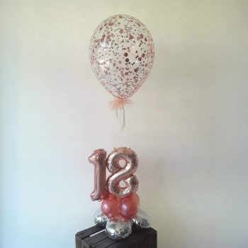 Ballon-Arrangement mit einem großen Konfettiballon in Rosé-Tönen und einer 18 aus roséfarbenen Zahlenballons auf kleiner Ballonbasis.
