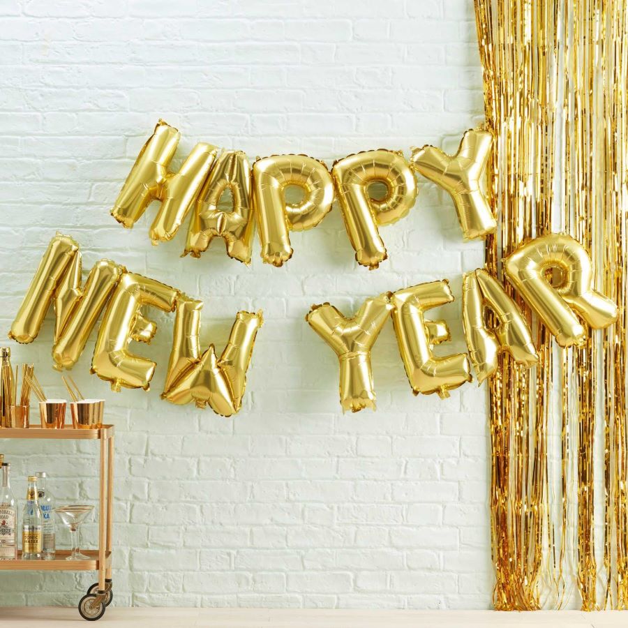 Goldene Folienballons in Buchstabenform mit der Aufschrift Happy New Year vor weißer Wand.