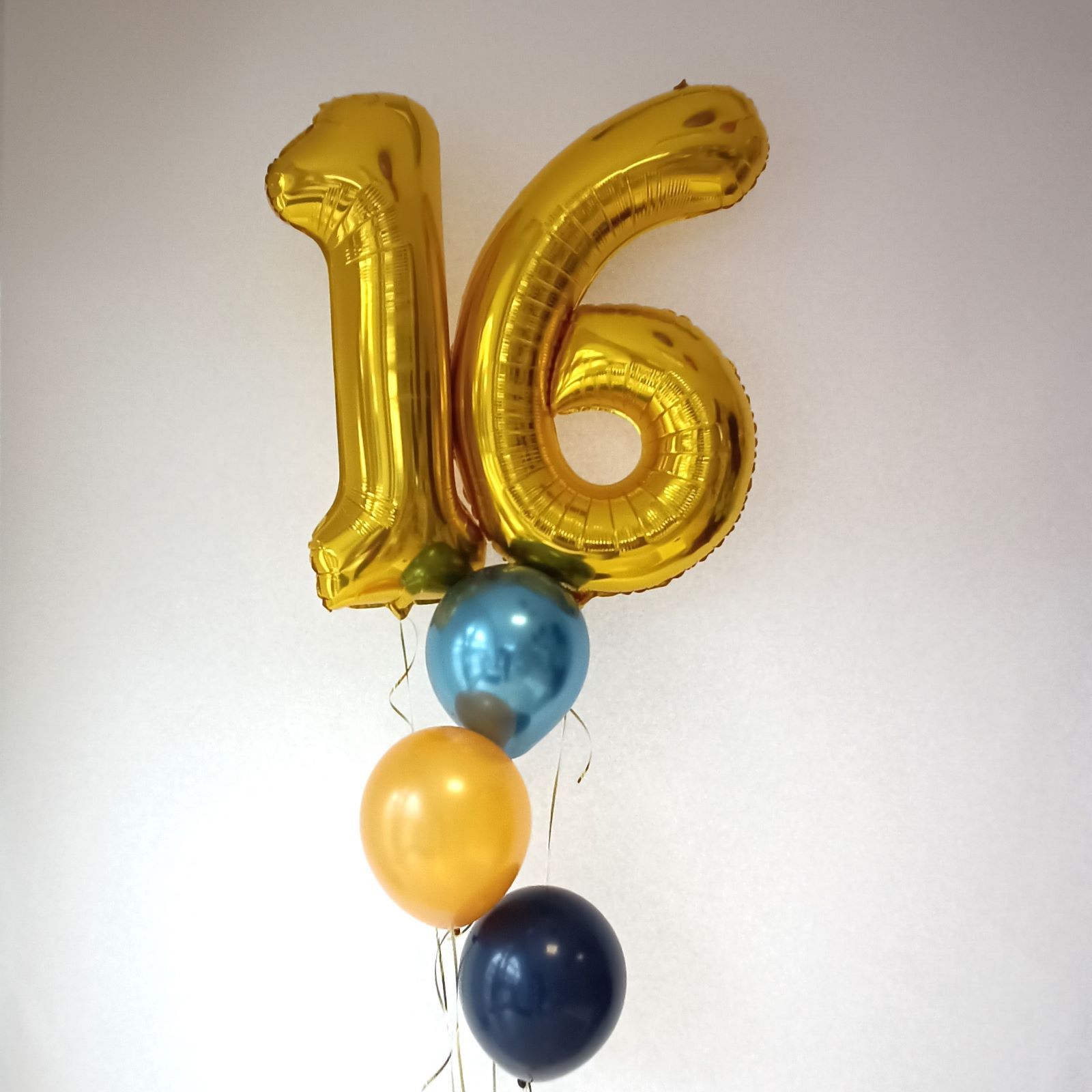 Goldene Folienballons in Form der Zahlen 1 und 6 mit blauen, gelben und dunkelblauen Latexballons.