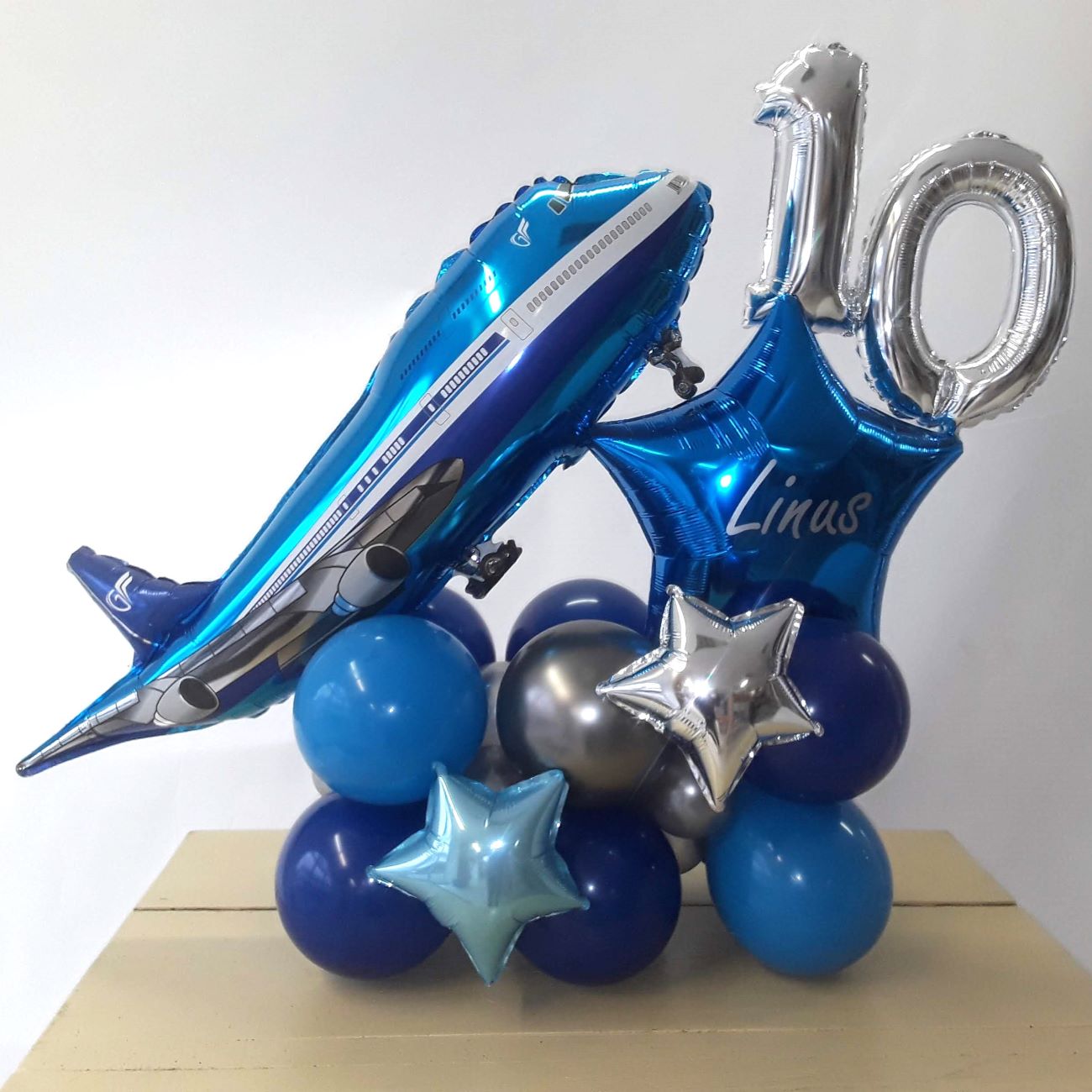 Ballonarrangement mit Flugzeug-Folienballon, Sternballons in Silber und Blau, Zahlenballons 1 und 0 und blauem, personalisiertem Namens-Stern-Ballon.