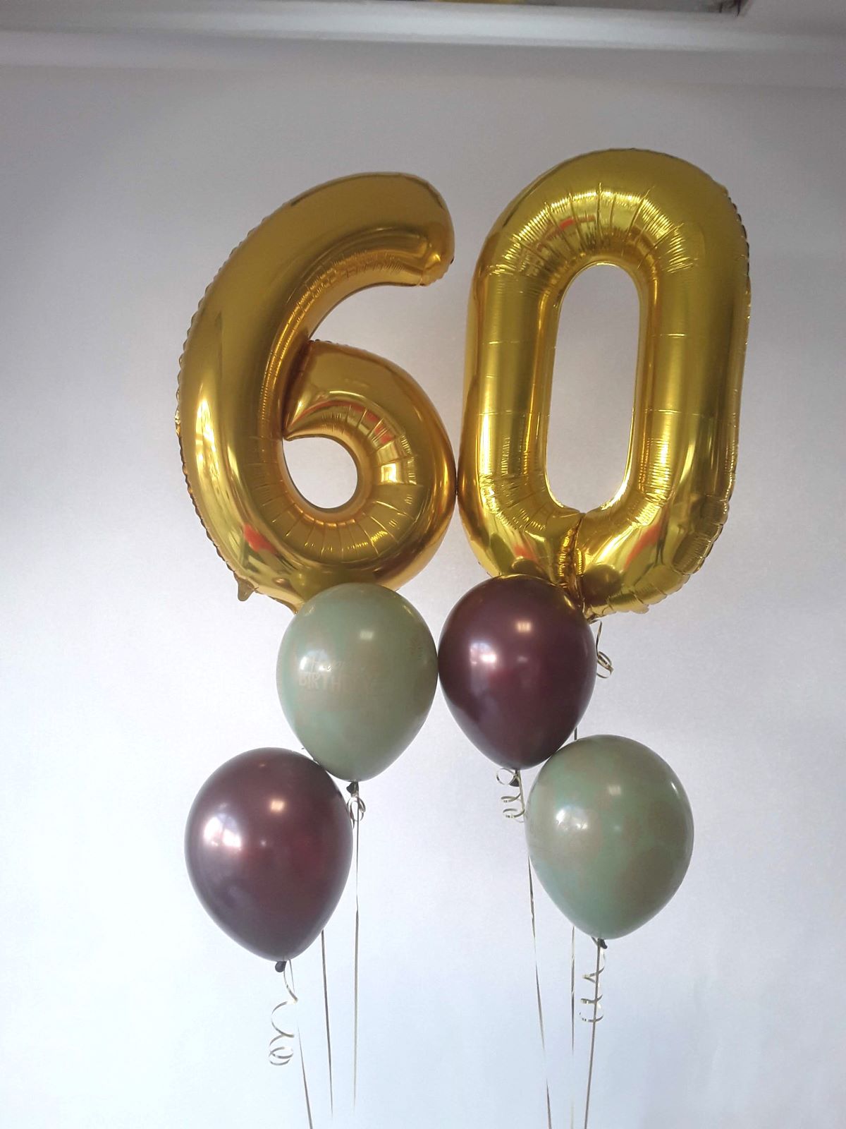 Goldene Folienballons in Form der Zahlen 6 und 0 mit grünen und bordeauxfarbenen Latexballons.