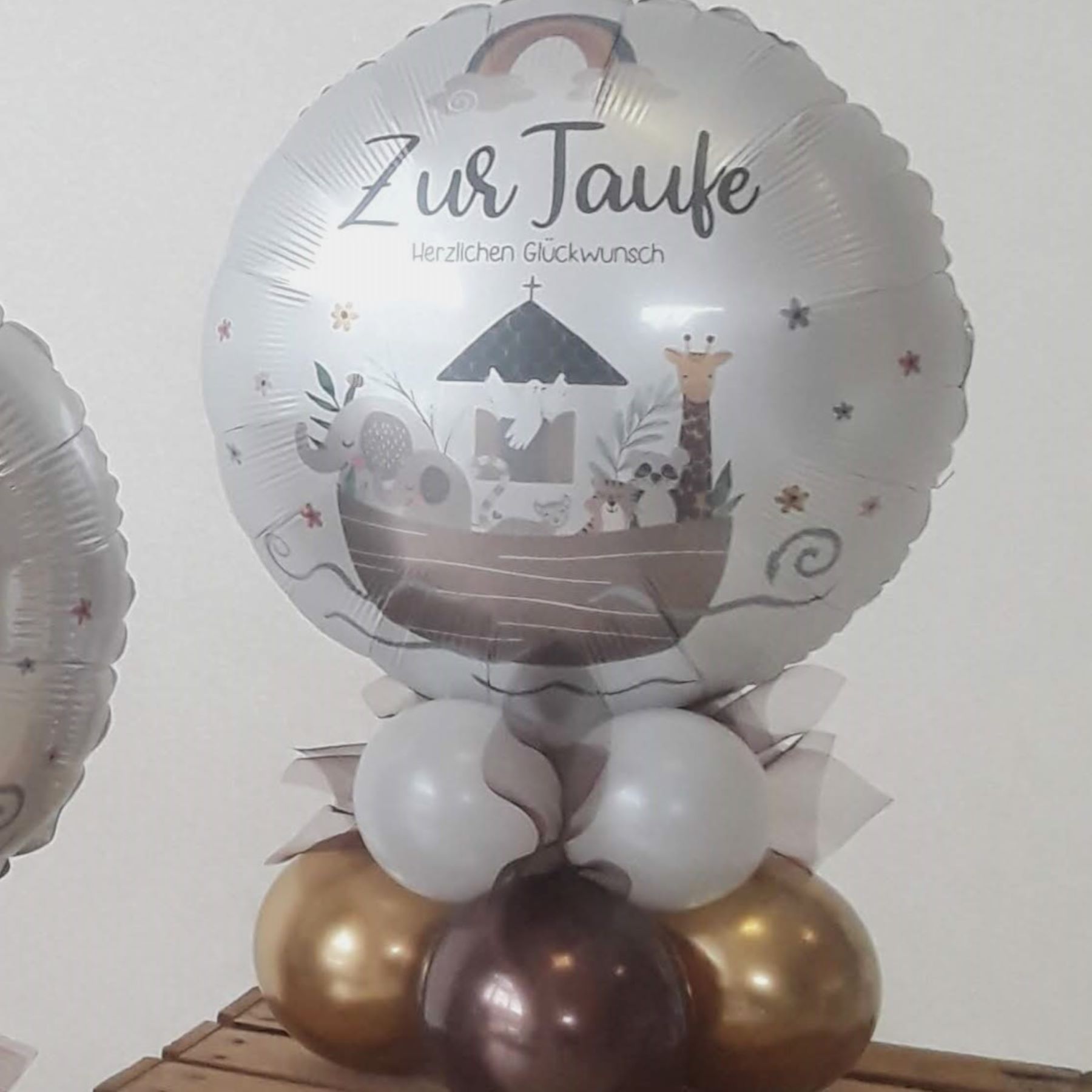 Silberner runder Folienballon mit Aufdruck 'Zur Taufe – Herzlichen Glückwunsch' und Arche Noah Motiv, auf Basis aus goldenen und weißen Luftballons.2