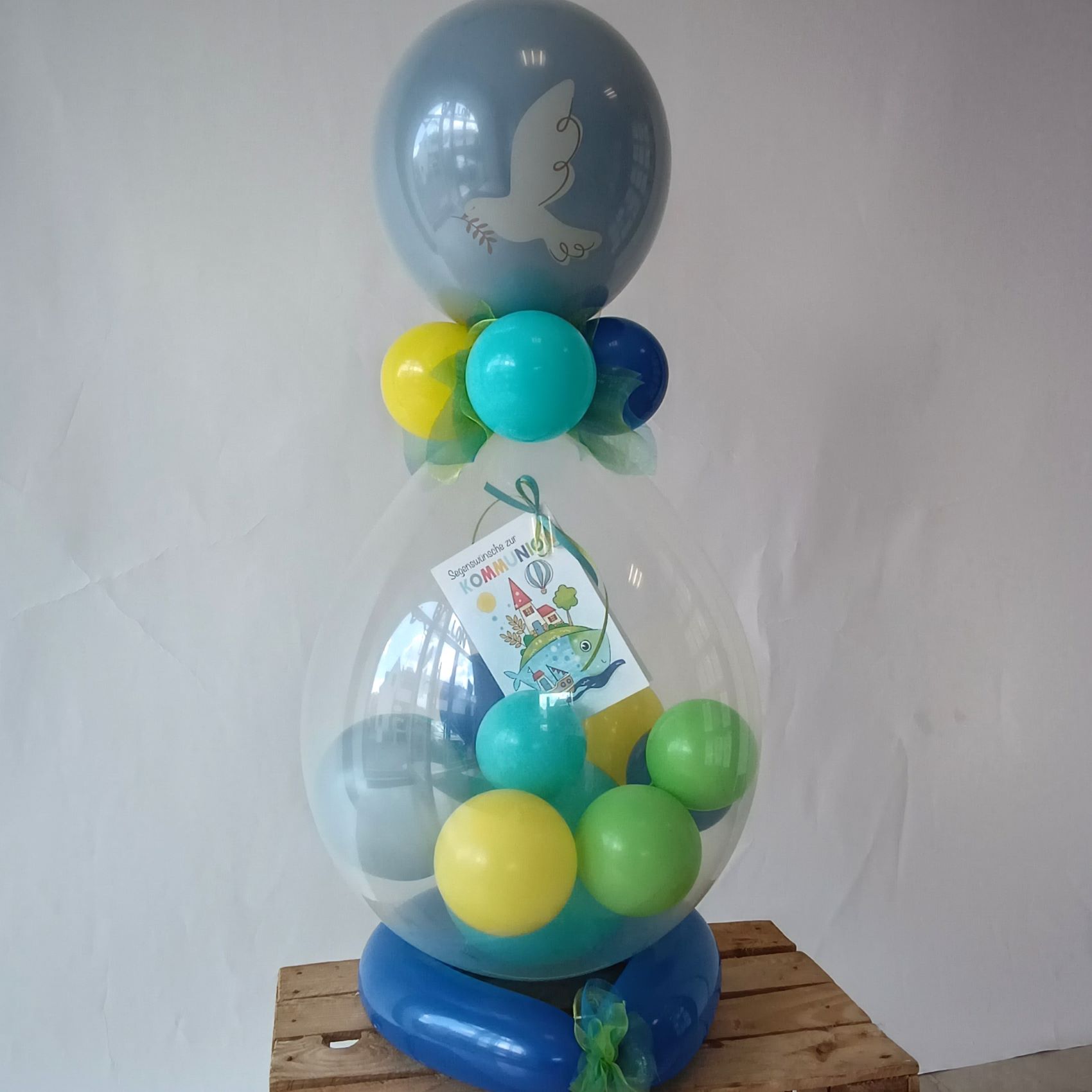 Großer Ballon mit blauer Taube, gefüllt mit bunten Ballons und Karte, auf blauer Basis