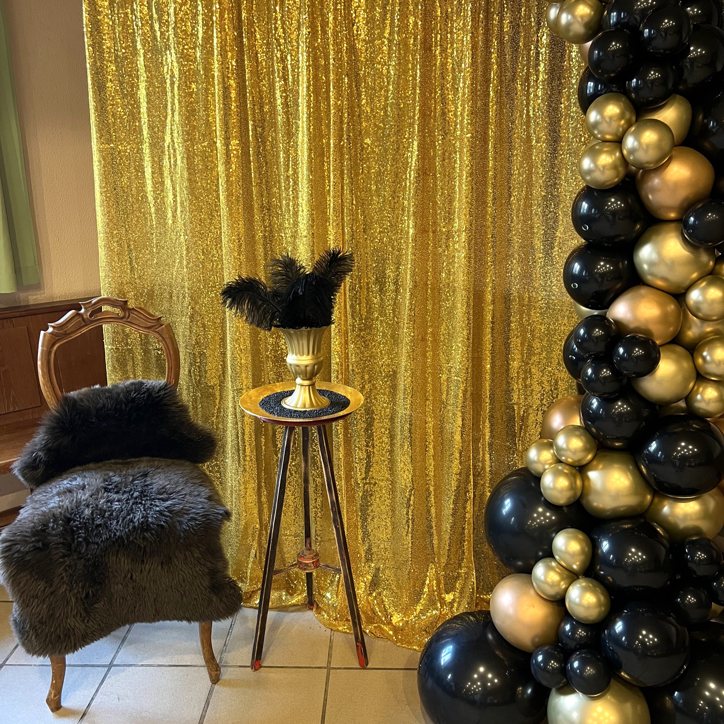 Schwarz-goldener Ballon-Halbbogen neben goldenem Vorhang und Dekoset auf Boden.