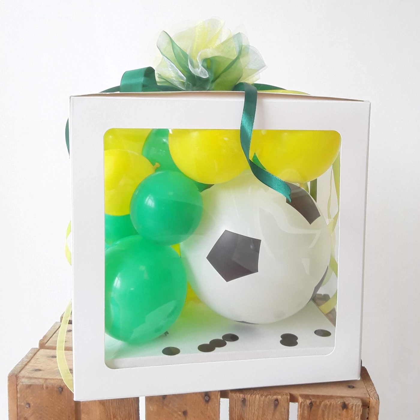 Ballonbox mit grün-gelben Luftballons und Fußball-Ballon, dekoriert mit grünem Schleifenband und Konfetti.