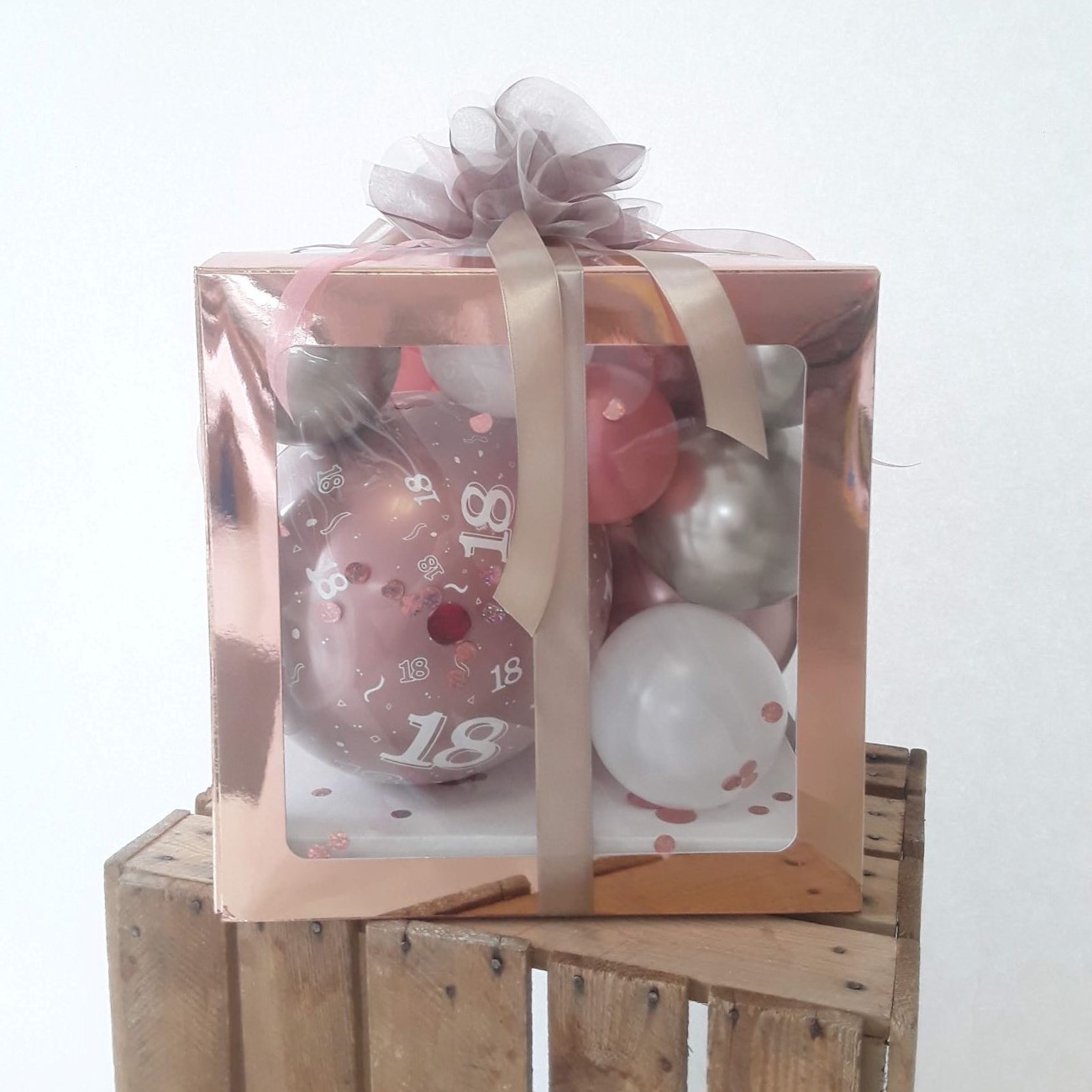 Ballonbox mit metallischer roséfarbener Hülle, gefüllt mit Luftballons in Rosé, Weiß und Silber, Konfetti und 18er-Aufdruck Ballon.