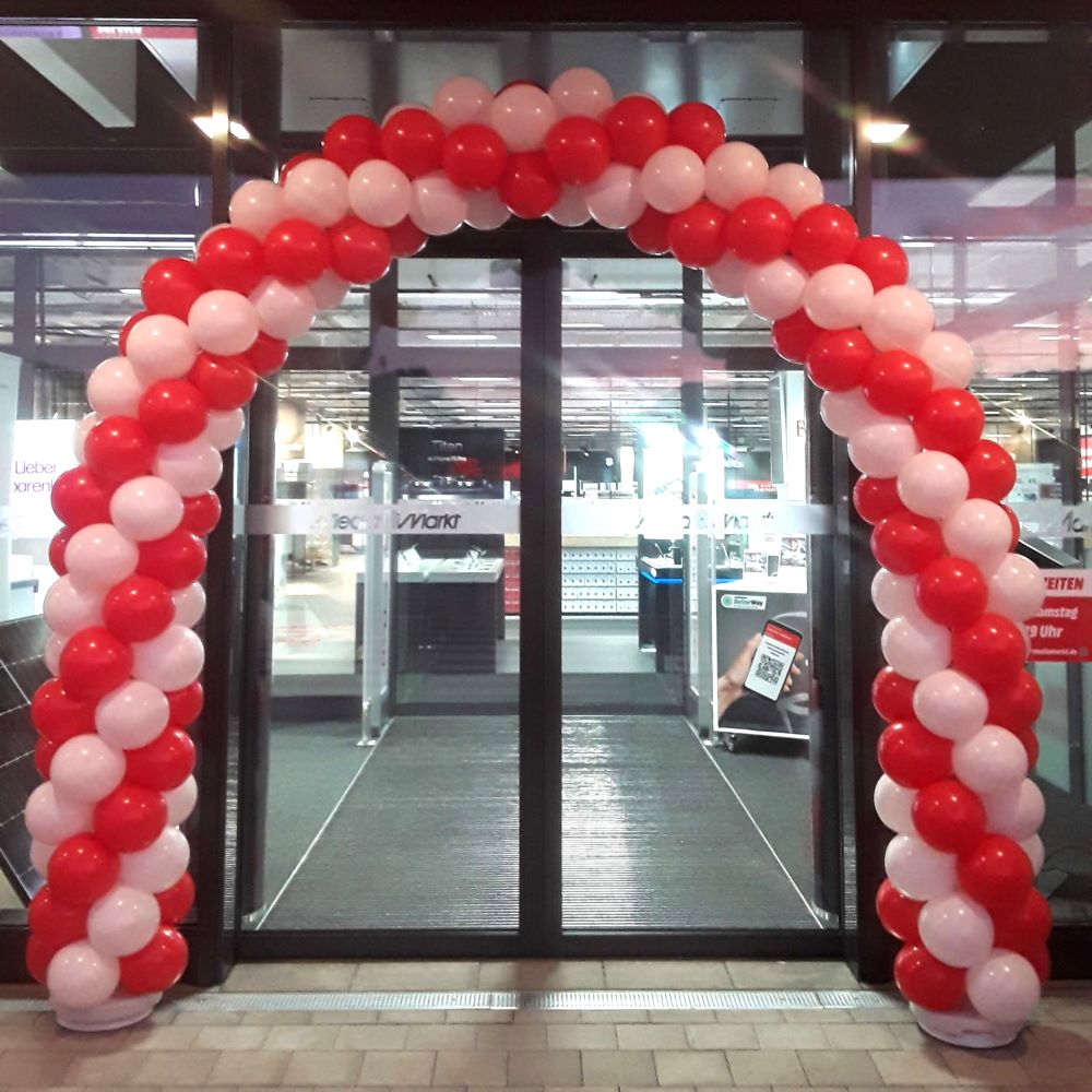 Gedrehter Ballonbogen in Rot und Weiß über einem automatischen Eingang