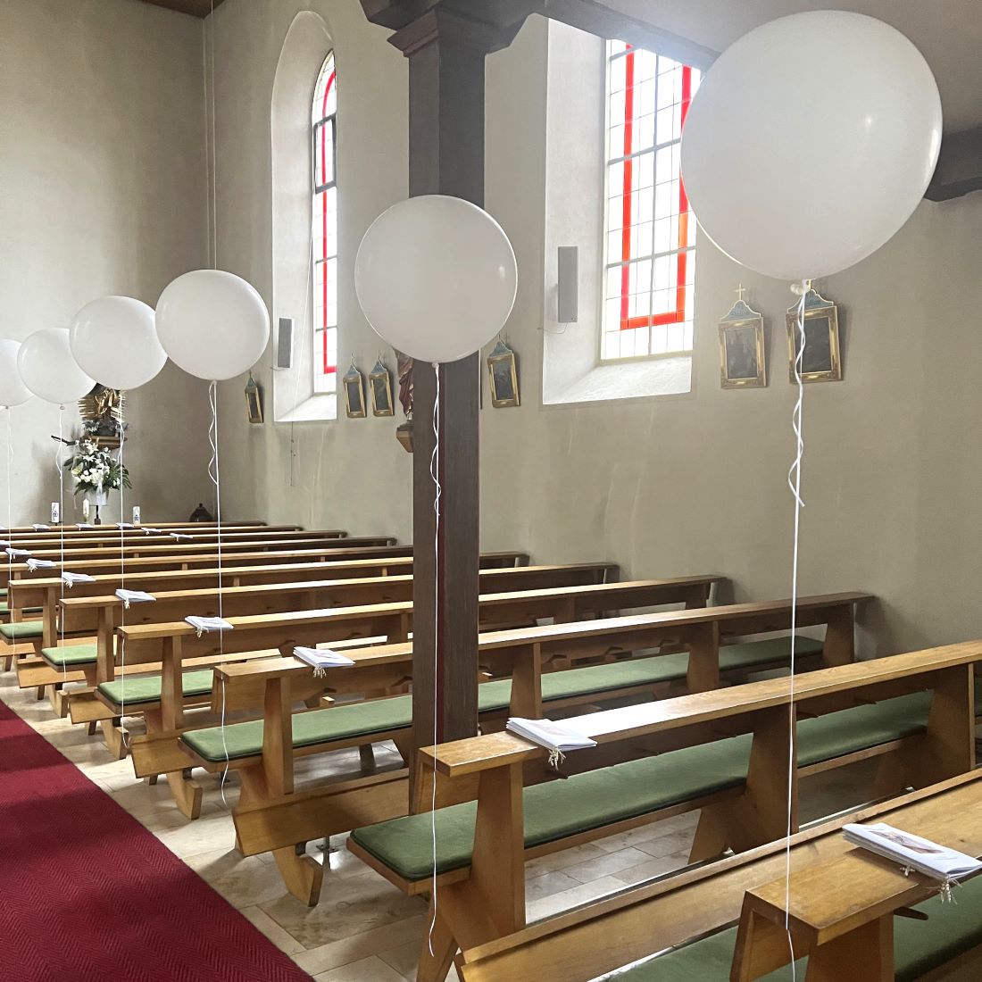 Mehrere große weiße Heliumballons mit langen weißen Satinbändern, die über die Kirchenbänke gekreuzt gespannt sind.