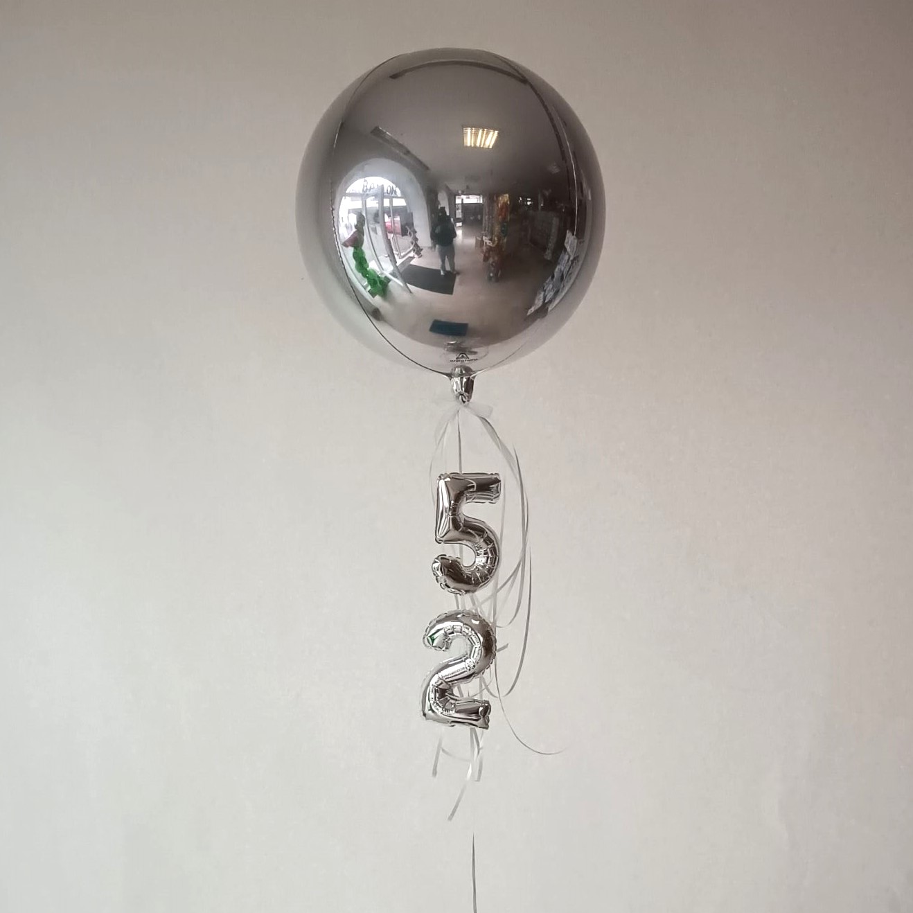 Große, silberne Ballonkugel mit schwebenden silbernen Zahlenballons 5 und 2.