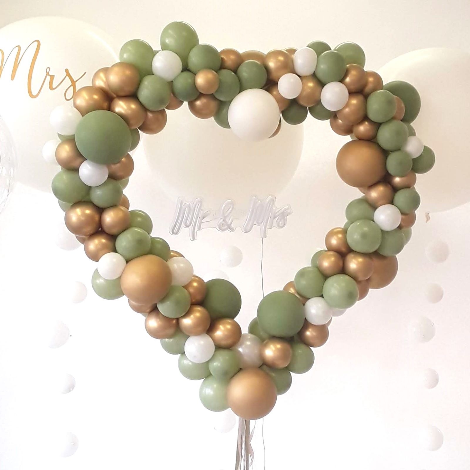 Herzförmiger Ballonbogen in vielen Farben mit unterschiedlich großen Ballons dekoriert und „Mr & Mrs“-Schriftzug in der Mitte grün gold
