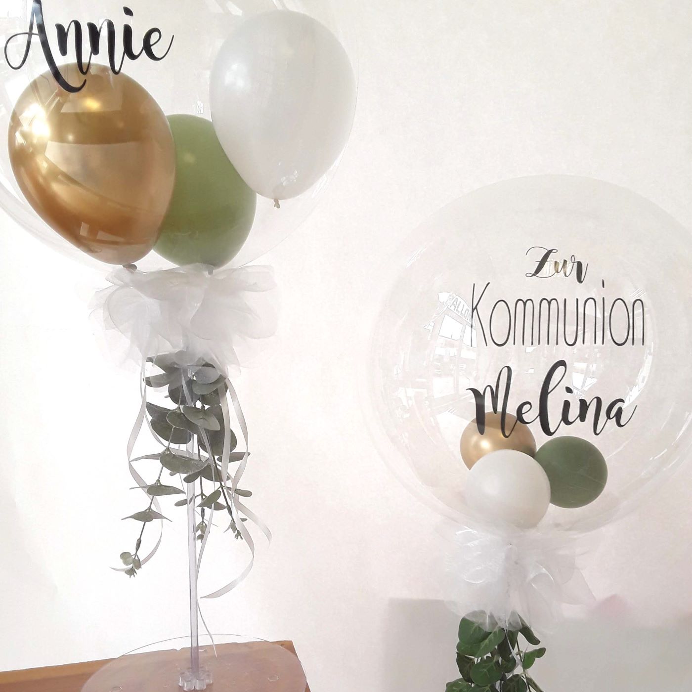 Zwei Tischständer-Bubbleballons mit grün-gold-weißen Ballons und personalisiertem Aufdruck 'Zur Kommunion Melina' und 'Zur Kommunion Annie'