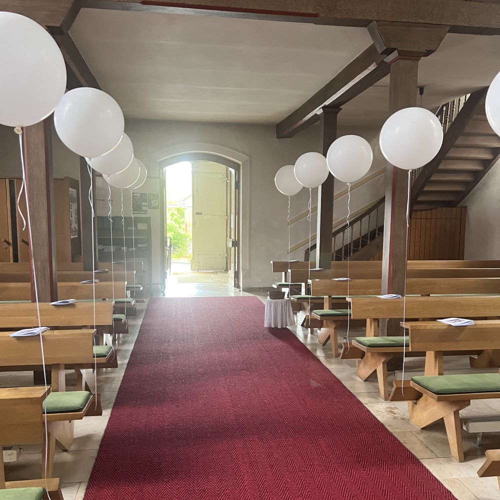 Mehrere große weiße Heliumballons mit langen weißen Satinbändern, die über die Kirchenbänke gekreuzt gespannt sind.-2