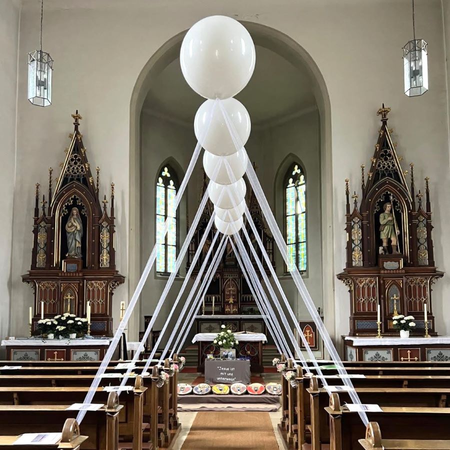 Reihe schwebender weißer Heliumballons mit Bändern, die beidseitig des roten Teppichs in einer Kirche angeordnet sind.-3