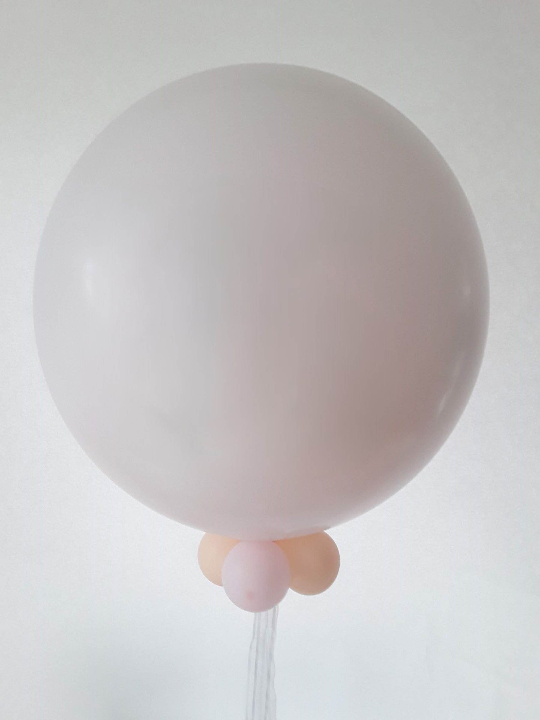Zart cremefarbener Riesenballon (60 cm) gefüllt mit ca. 30 kleinen Innenballons in Rosa- und Cremetönen, dekoriert mit drei kleinen Ballons in Pastellfarben am Ballonhals