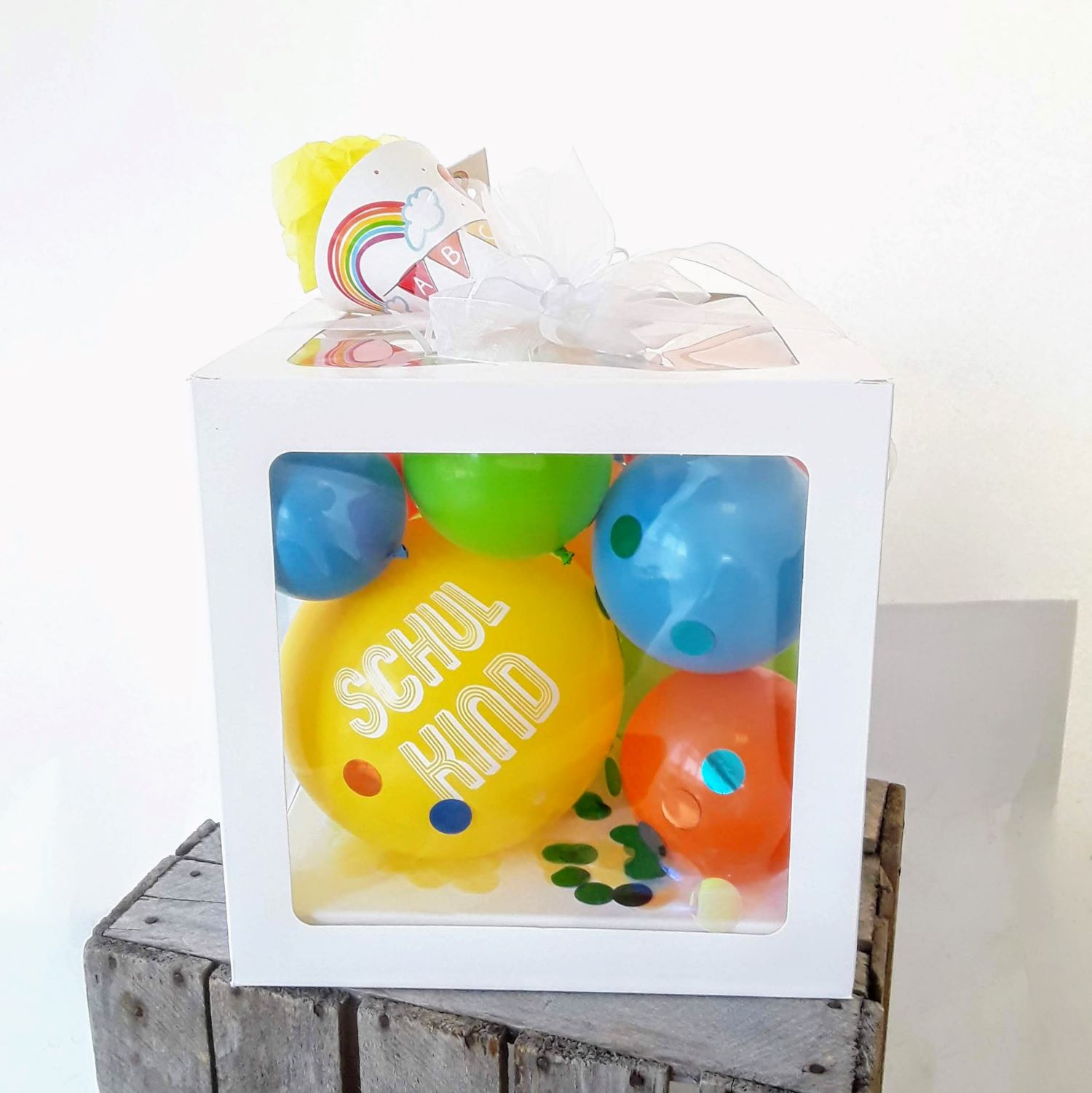 Ballonbox mit bunten Latexballons und gelbem Ballon mit Aufdruck 'Schulkind', dekoriert mit Konfetti