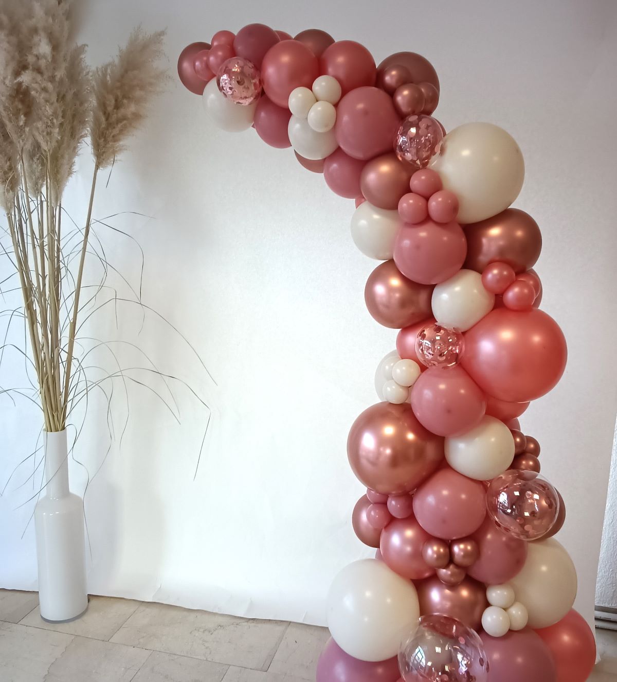 Ballon-Halbbogen in metallic rosa, creme mit Konfetti-Ballons neben Pamapasgras