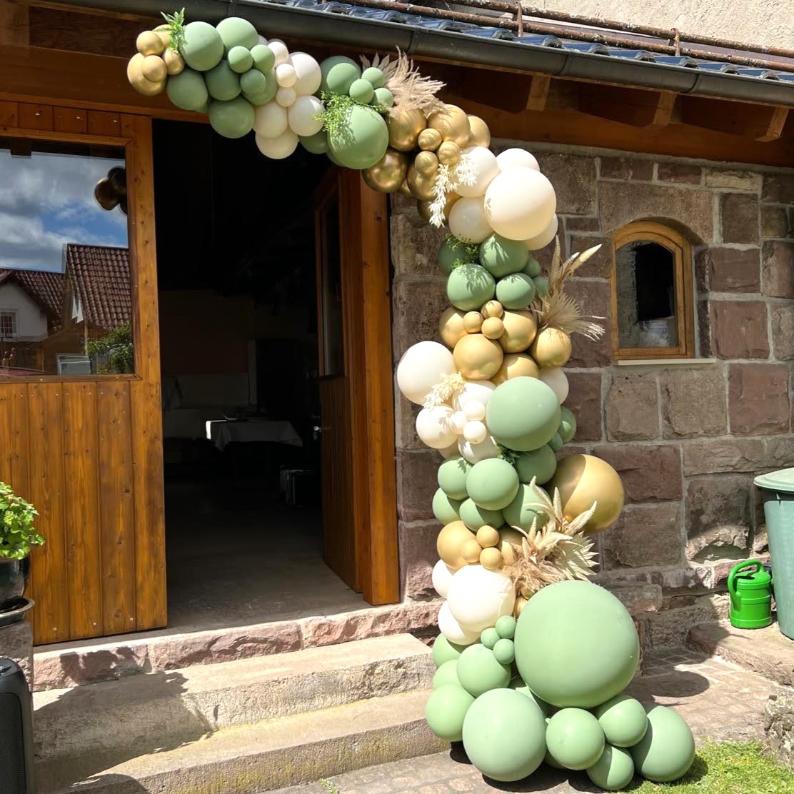 Eindrucksvolle Ballongirlande in Gold, Salbeigrün, Creme und Weiß, arrangiert um einen rustikalen Steineingang mit Holzrahmen2