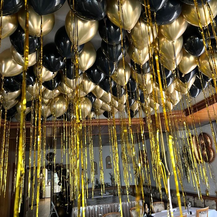 Schwarz-goldene Ballons an der Decke schwebend mit langen goldenen Bändern in einem Raum.