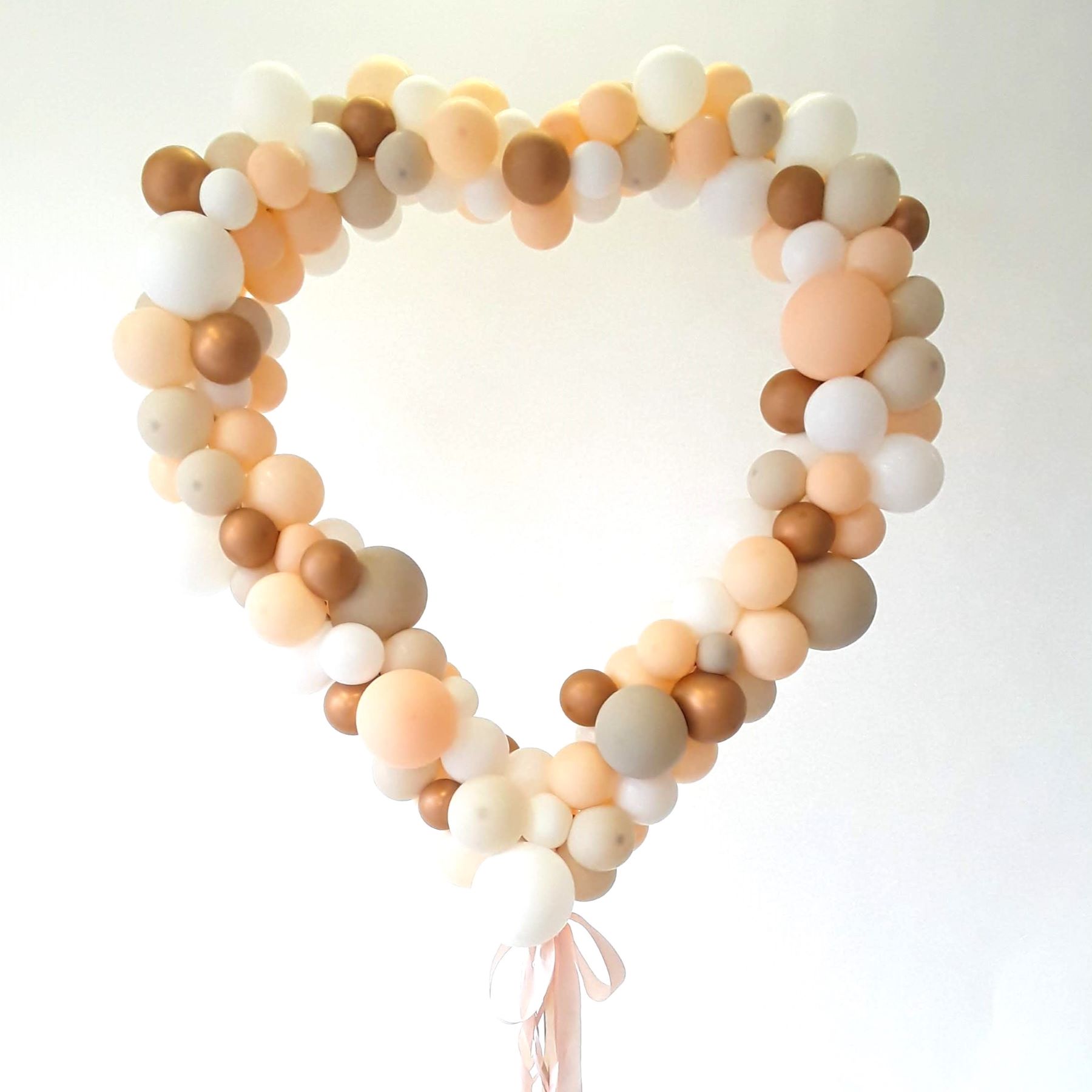 Herzförmige Ballondekoration aus Luftballons in verschiedenen Farben, gefüllt mit kleinen und großen Ballons, teilweise mit Metallic-Effekt, dekoriert auf einem Gestell, aprico.weiß