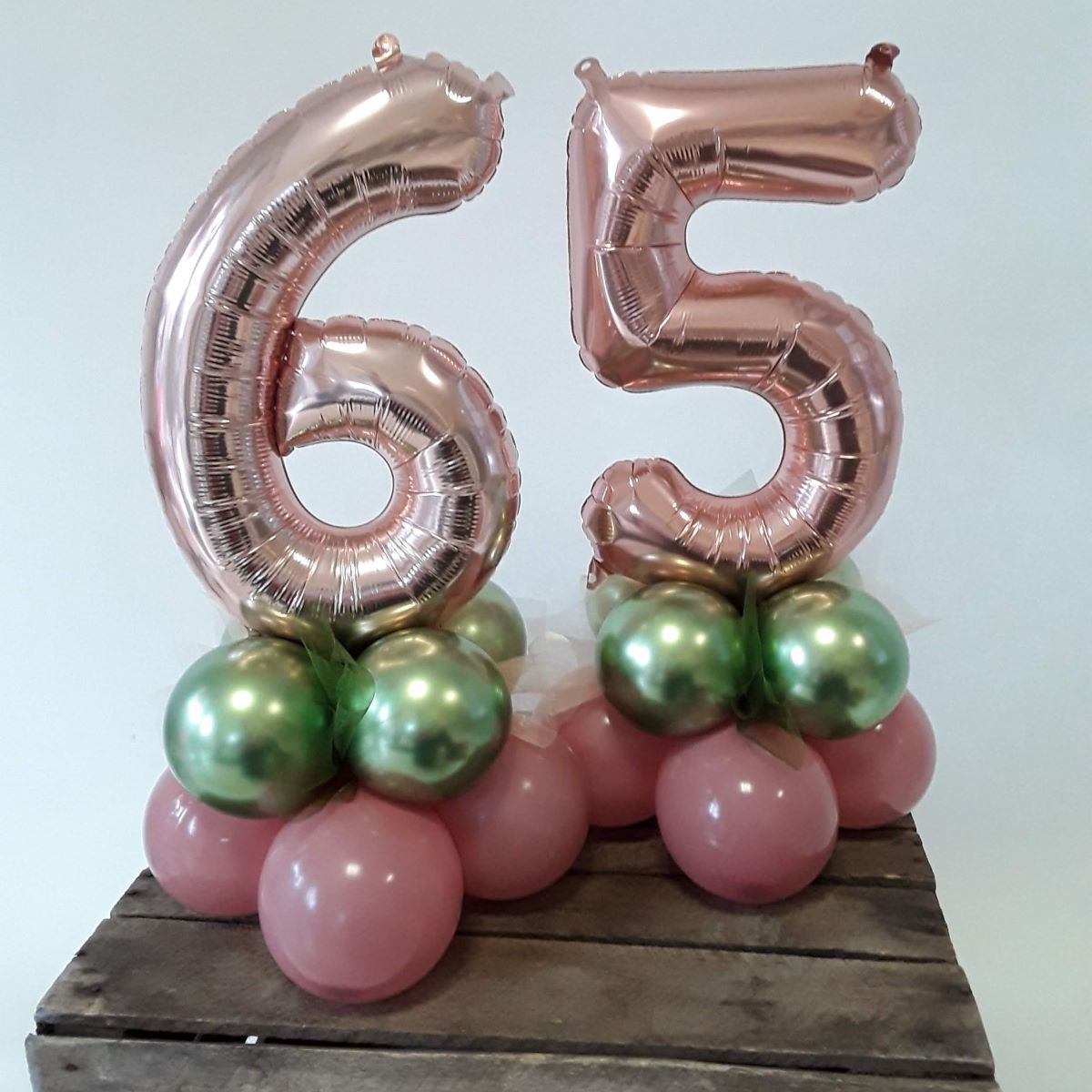 Ballon-Arrangement mit roséfarbenen Zahlenballons '6' und '5' auf einer Basis aus rosafarbenen und grün glänzenden Latexballons.