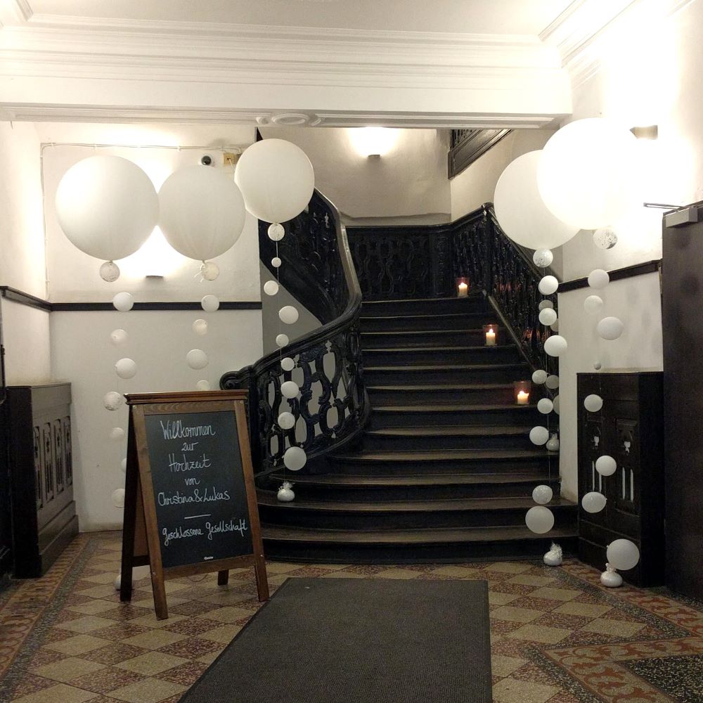 Elegante Raumdekoration mit großen weißen Ballons in verschiedenen Größen, schwebend und als Girlanden arrangiert, an Treppenaufgang