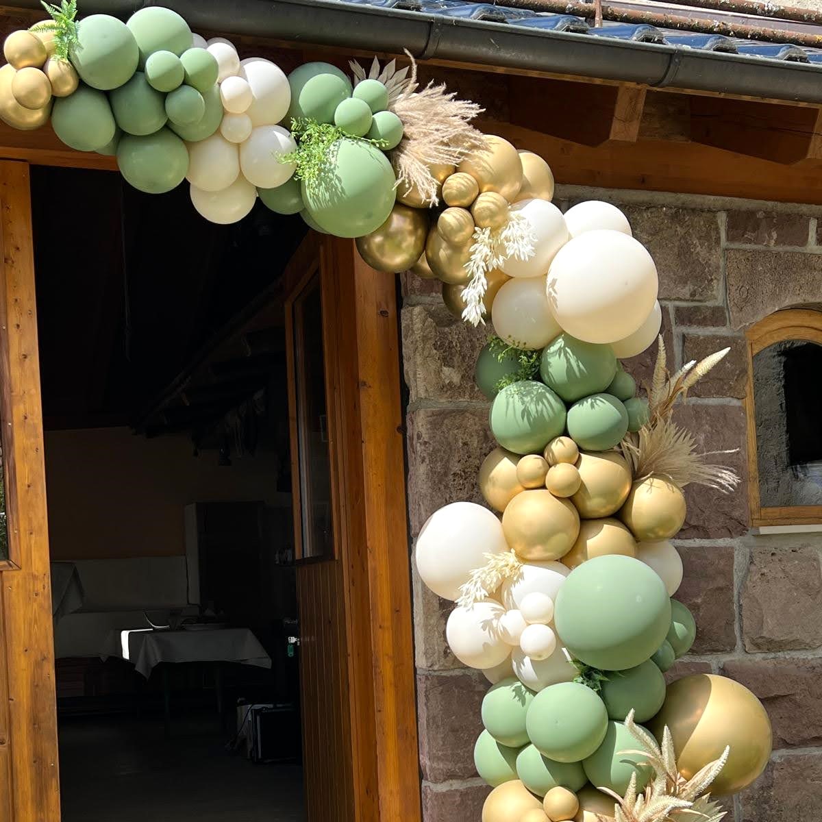 Eindrucksvolle Ballongirlande in Gold, Salbeigrün, Creme und Weiß, arrangiert um einen rustikalen Steineingang mit Holzrahmen