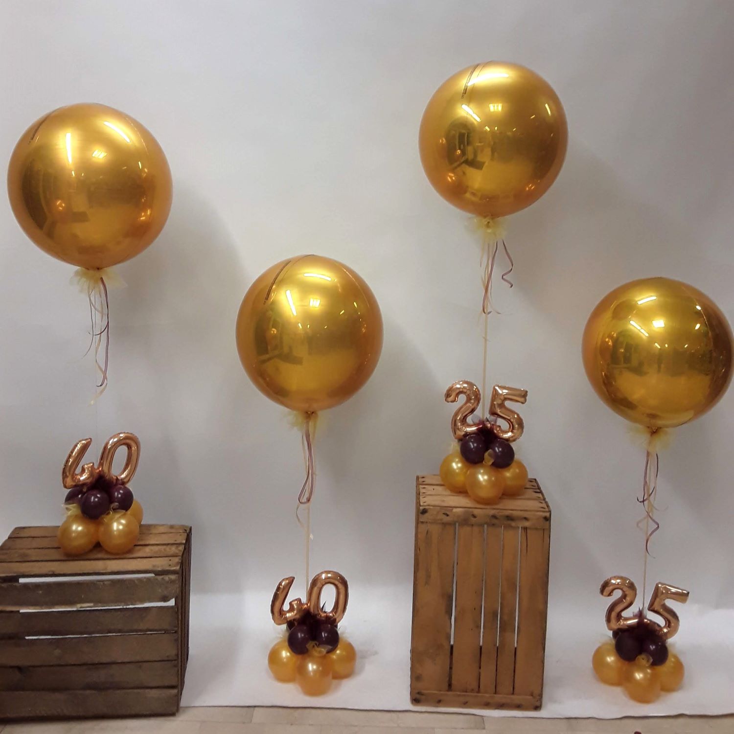 Ballonarrangements mit glänzenden goldenen Kugelballons und kleinen Zahlenballons '25' und '40' auf Ballonfüßen