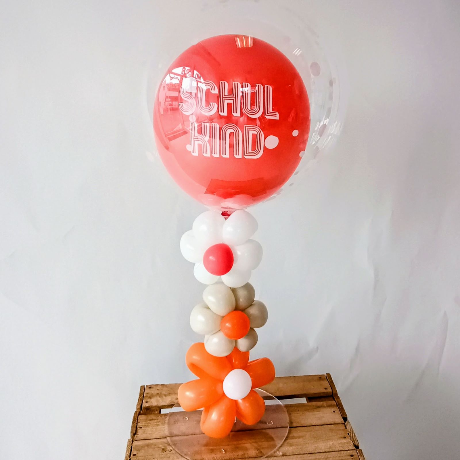 Ballon-Bubble in transparent mit rotem Innenballon 'Schulkind', dekoriert mit weißen, beigen und orangen Ballonblumen