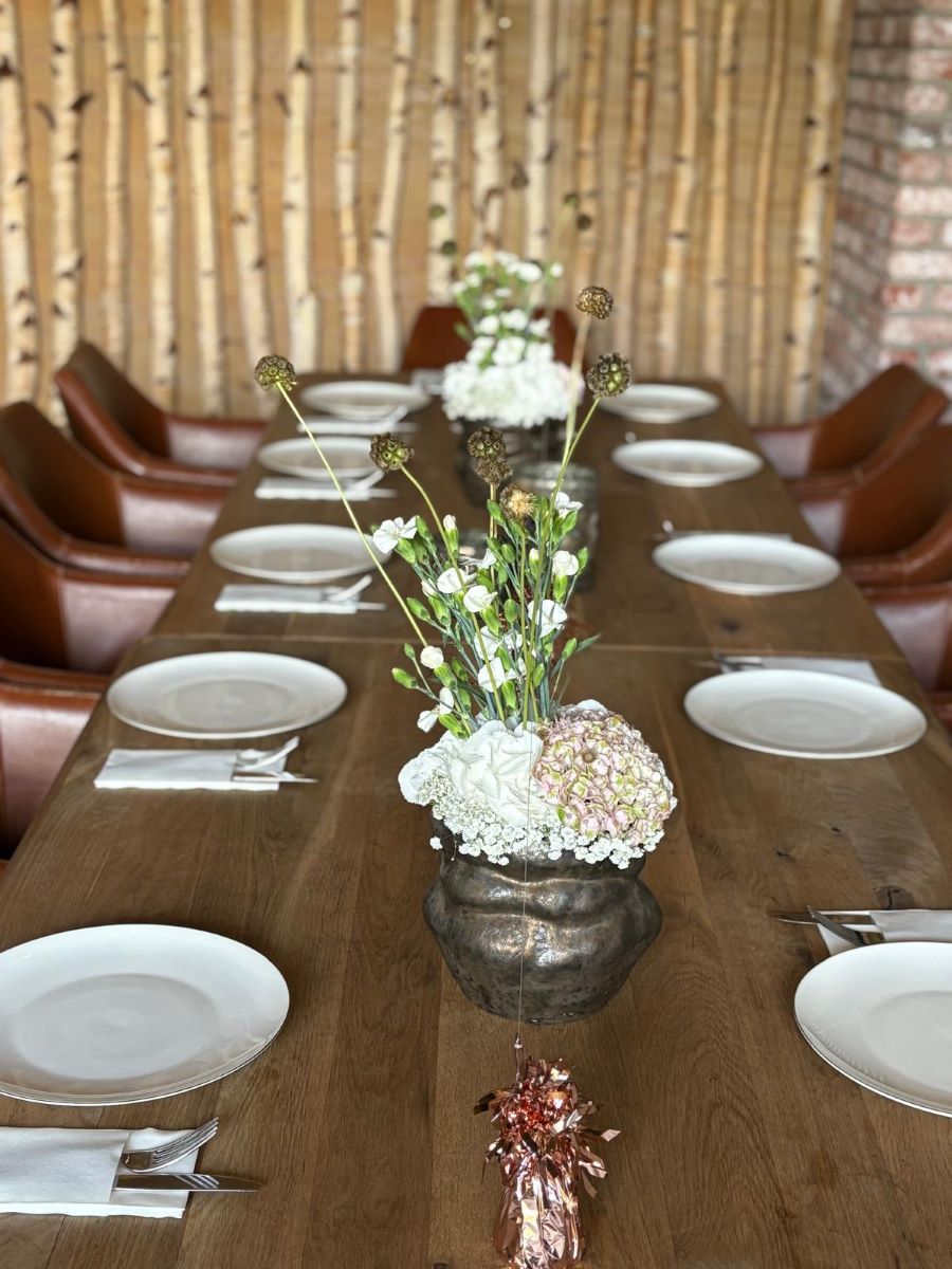Gedeckte Tafel mit Geschirr, Blumen und rosegoldenen Ballongewichten vor Holzwand