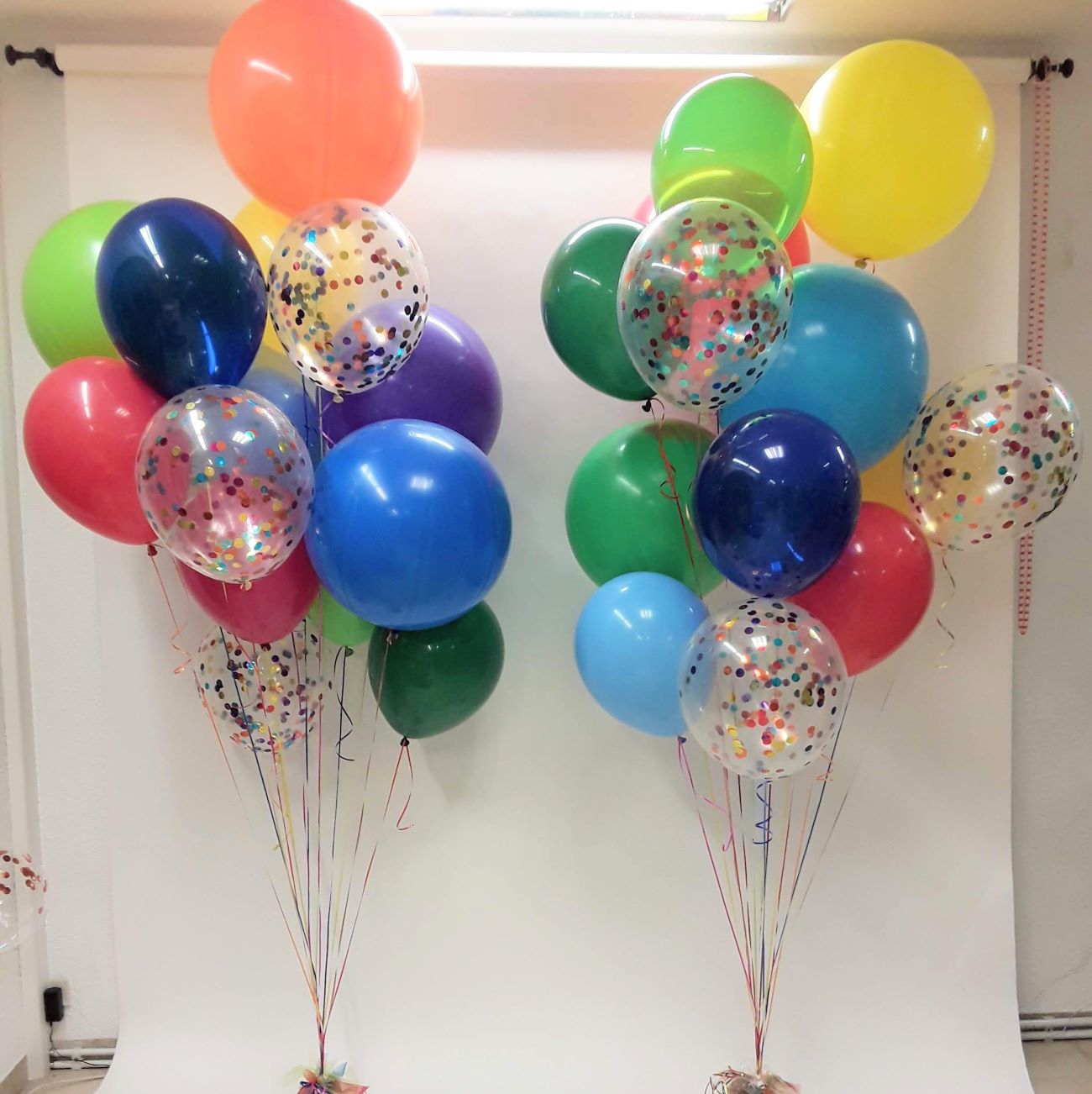 Zwei bunte Ballonbouquets mit Aufdruck 'Schulkind' und Konfettiballons, auf weißem Hintergrund fotografiert.