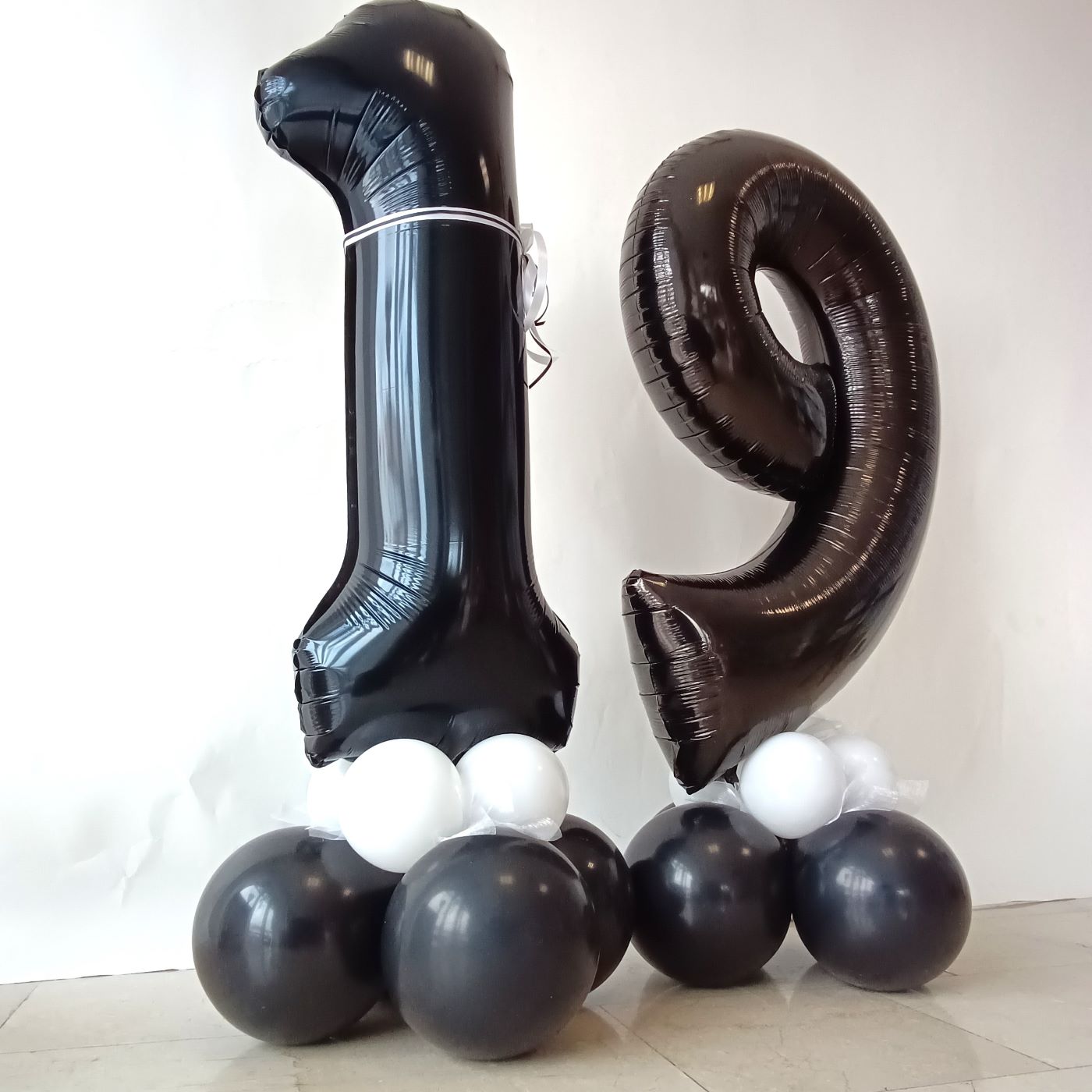 Zwei große schwarze Folienballons in Form der Zahl „1“ und „9“ auf schwarz-weißer Ballonbasis
