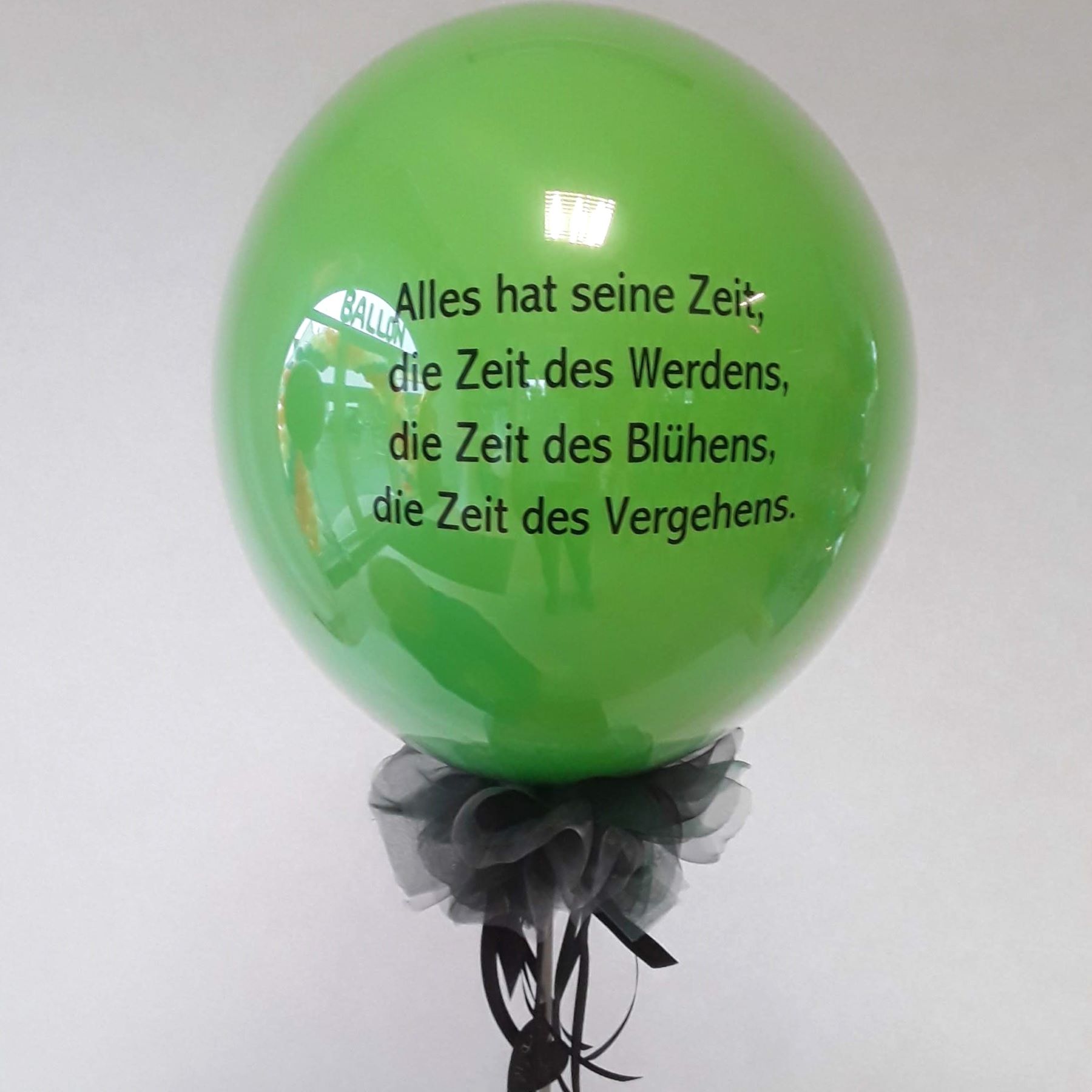 Großer grüner Ballon mit schwarzem Aufdruck 'Alles hat seine Zeit, die Zeit des Werdens, die Zeit des Blühens, die Zeit des Vergehens', dekoriert mit schwarzem Tüll am Ballonhals.
