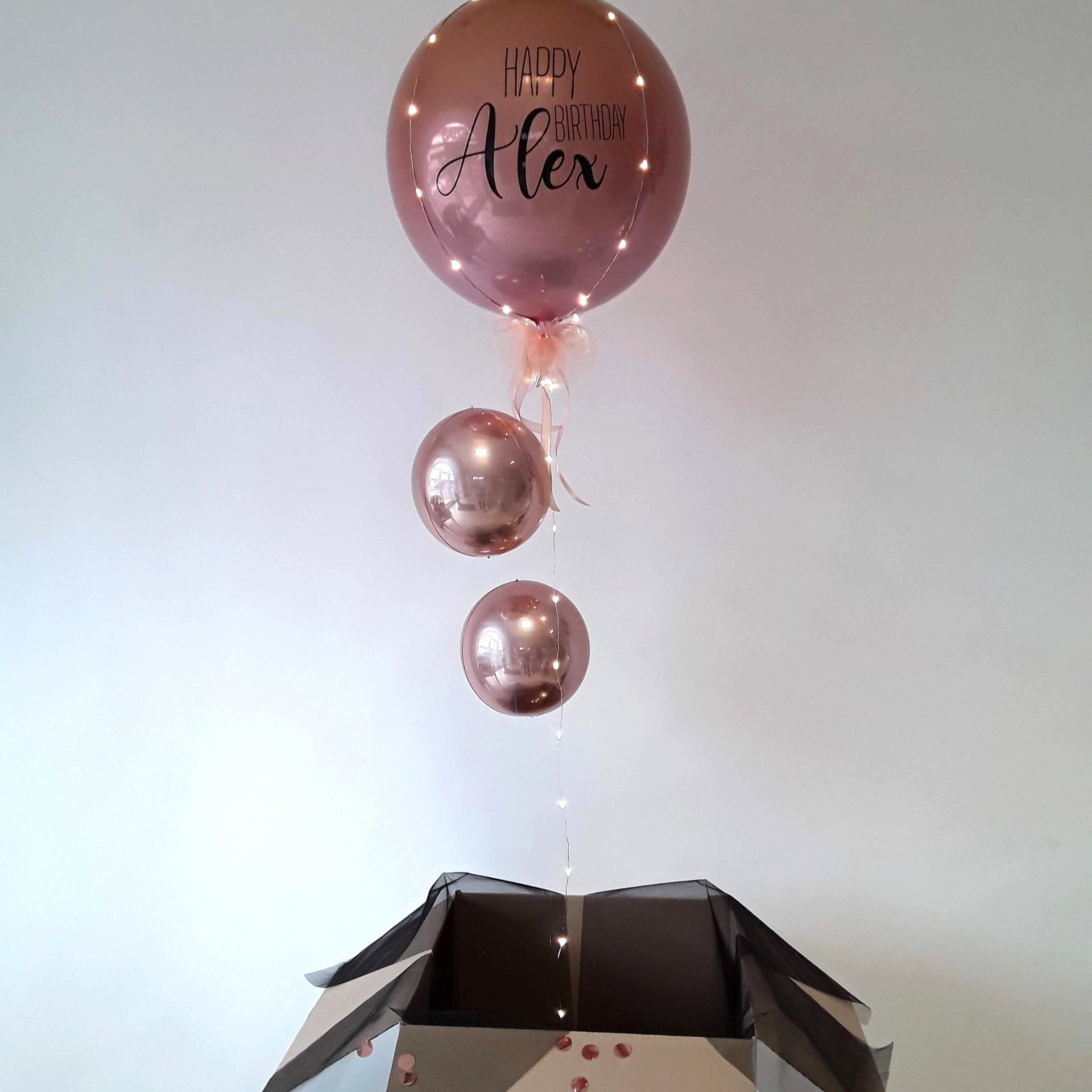 Kugelballon in Roségold mit schwarzem Aufdruck und Lichterkette, dekoriert für Geburtstag.