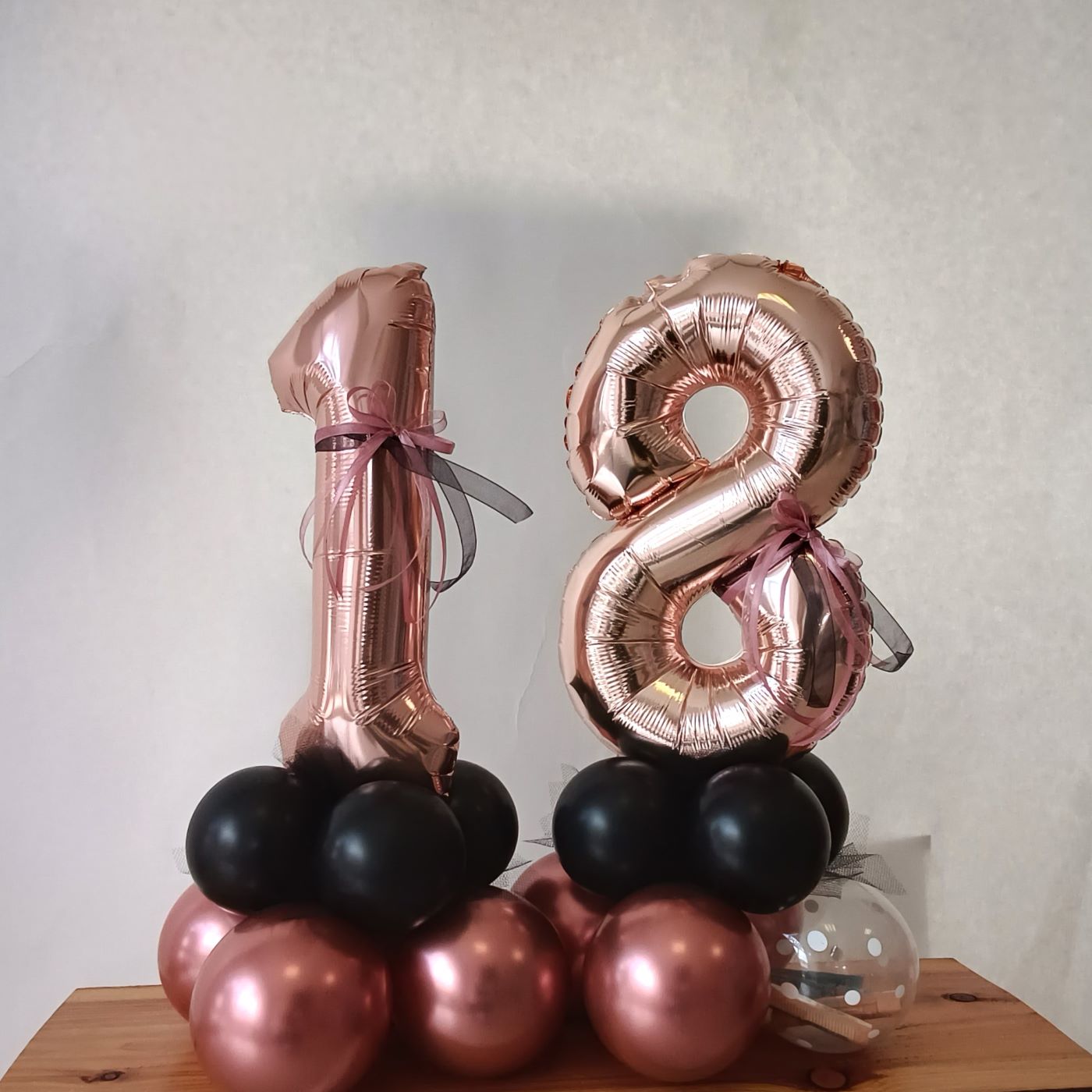 Zahlenballons 1 und 8 in Roségold auf einem Sockel aus schwarzen und roségoldenen Ballons