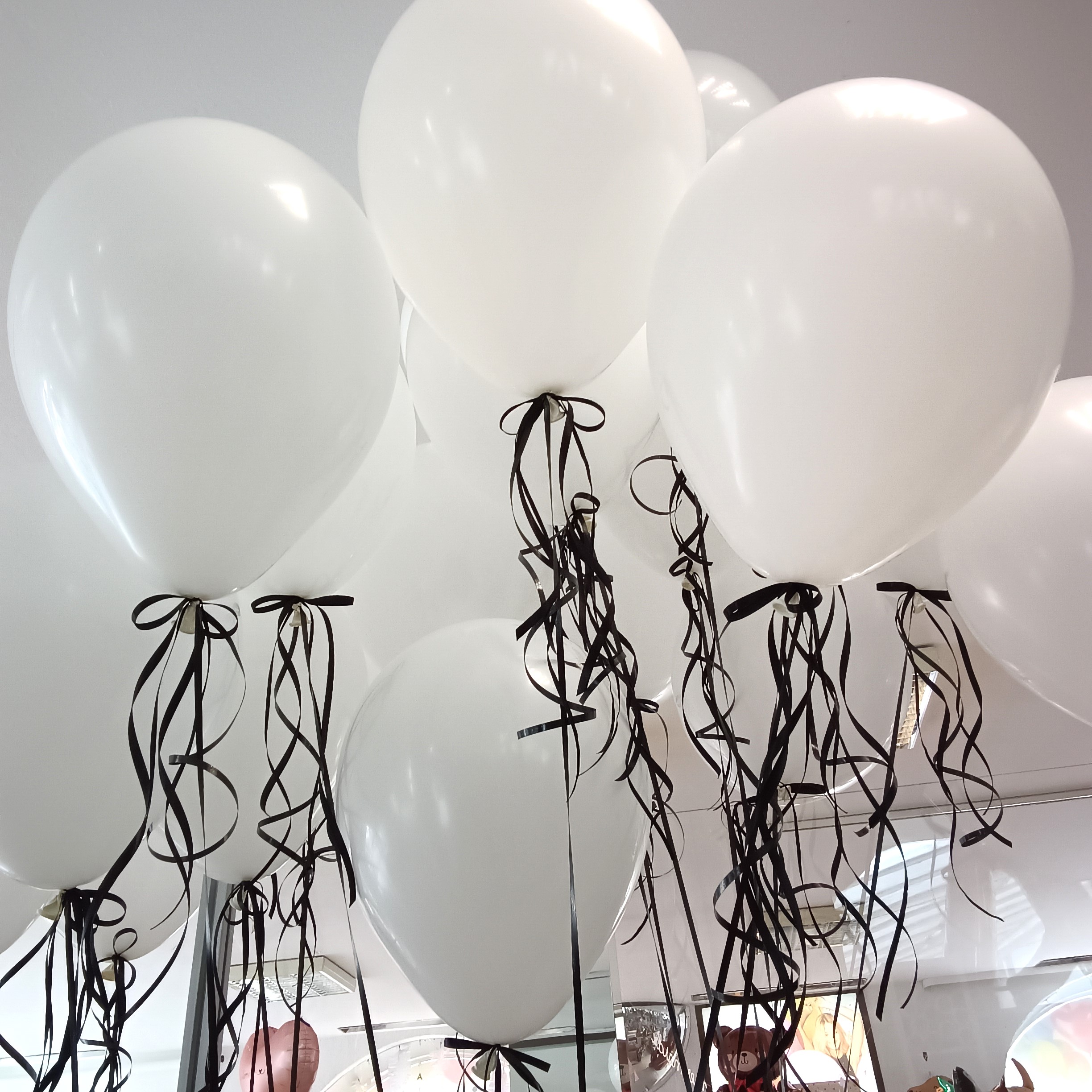weiße Heliumballons mit schwarzen Bändern, schwebend unter einer Zimmerdecke