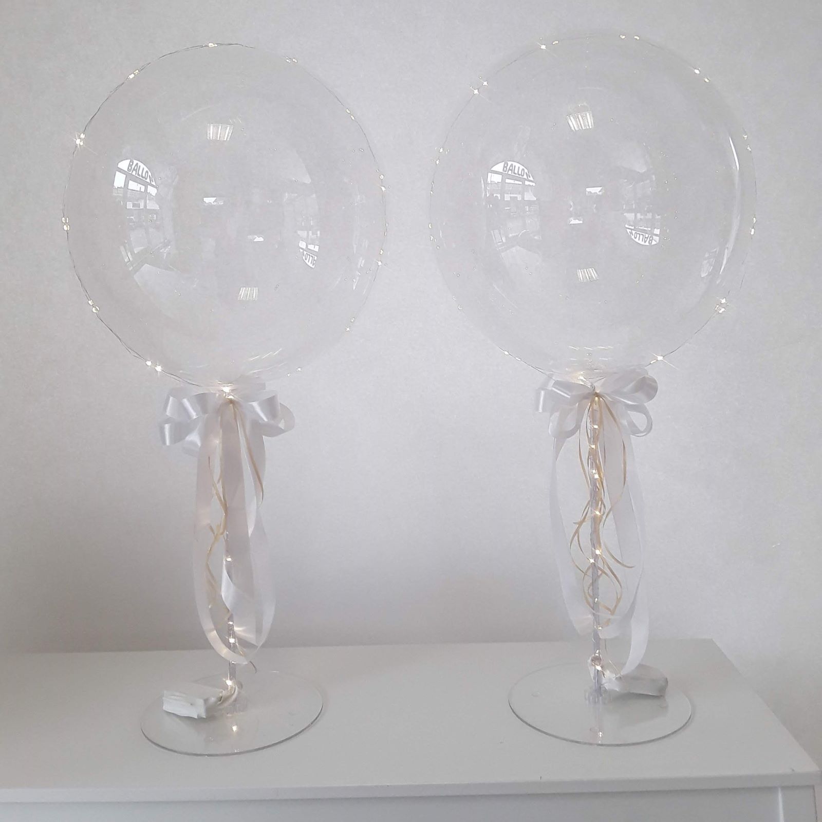 2 Transparente Ballons auf Tischständer mit weißer Schleife und Lichterkette