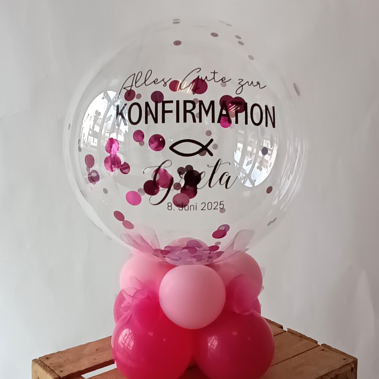 Transparenter Bubbleballon mit pinkem Konfetti, Aufdruck 'Alles Gute zur KONFIRMATION Greta 8. Juni 2025', auf rosa-pinker Ballonbasis