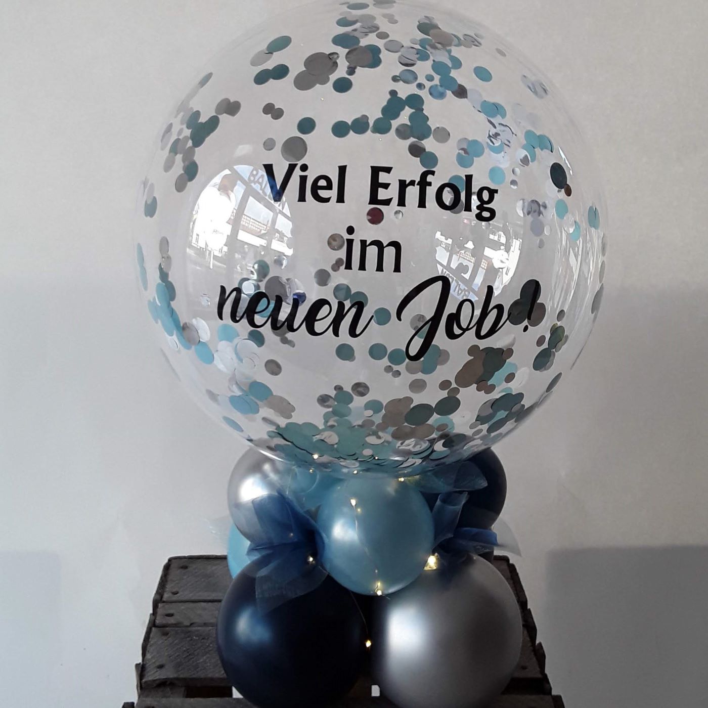 Bubble-Ballon mit blau-silbernem Konfetti und Aufdruck 'Viel Erfolg im neuen Job!', dekoriert mit blauen und silbernen Ballons als Tischbouquet.