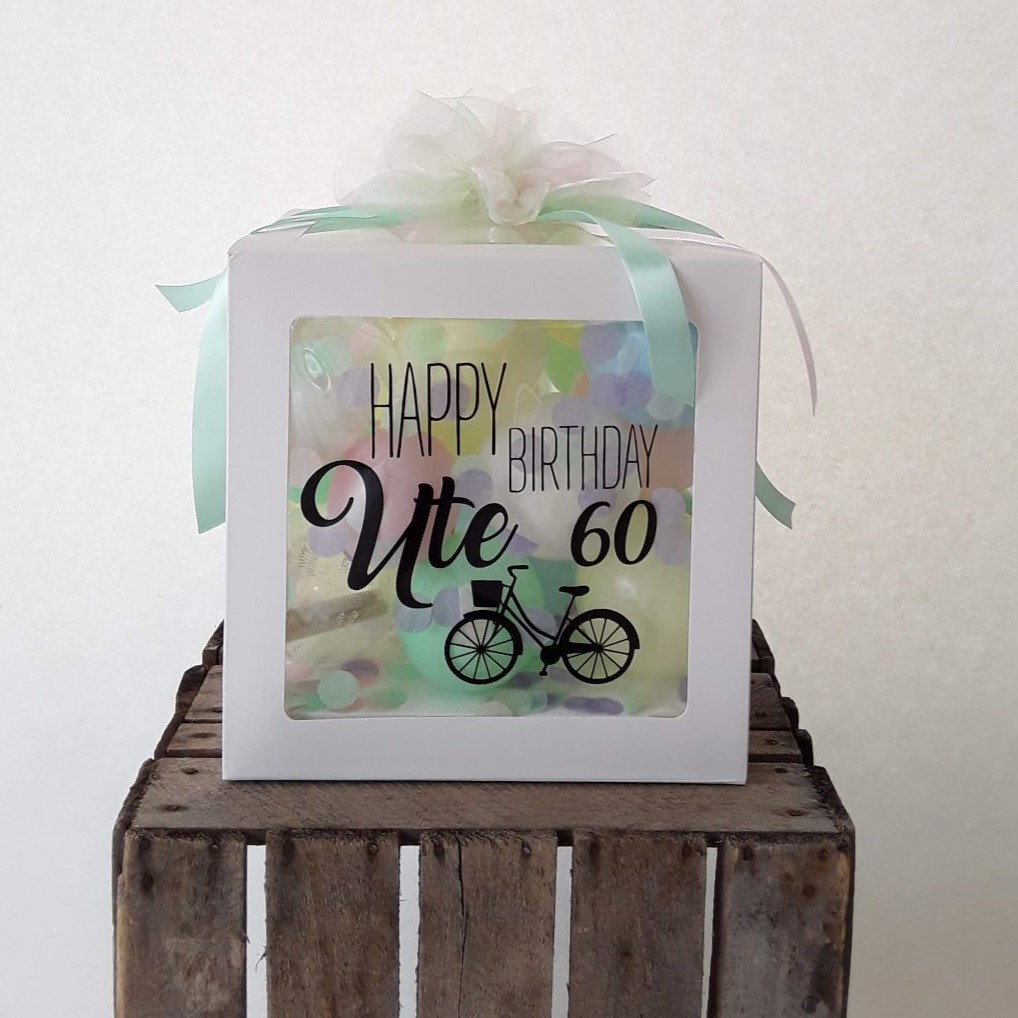 Ballonbox mit Aufdruck 'Happy Birthday Ute 60' und Fahrradmotiv, gefüllt mit pastellfarbenen Ballons und Konfetti