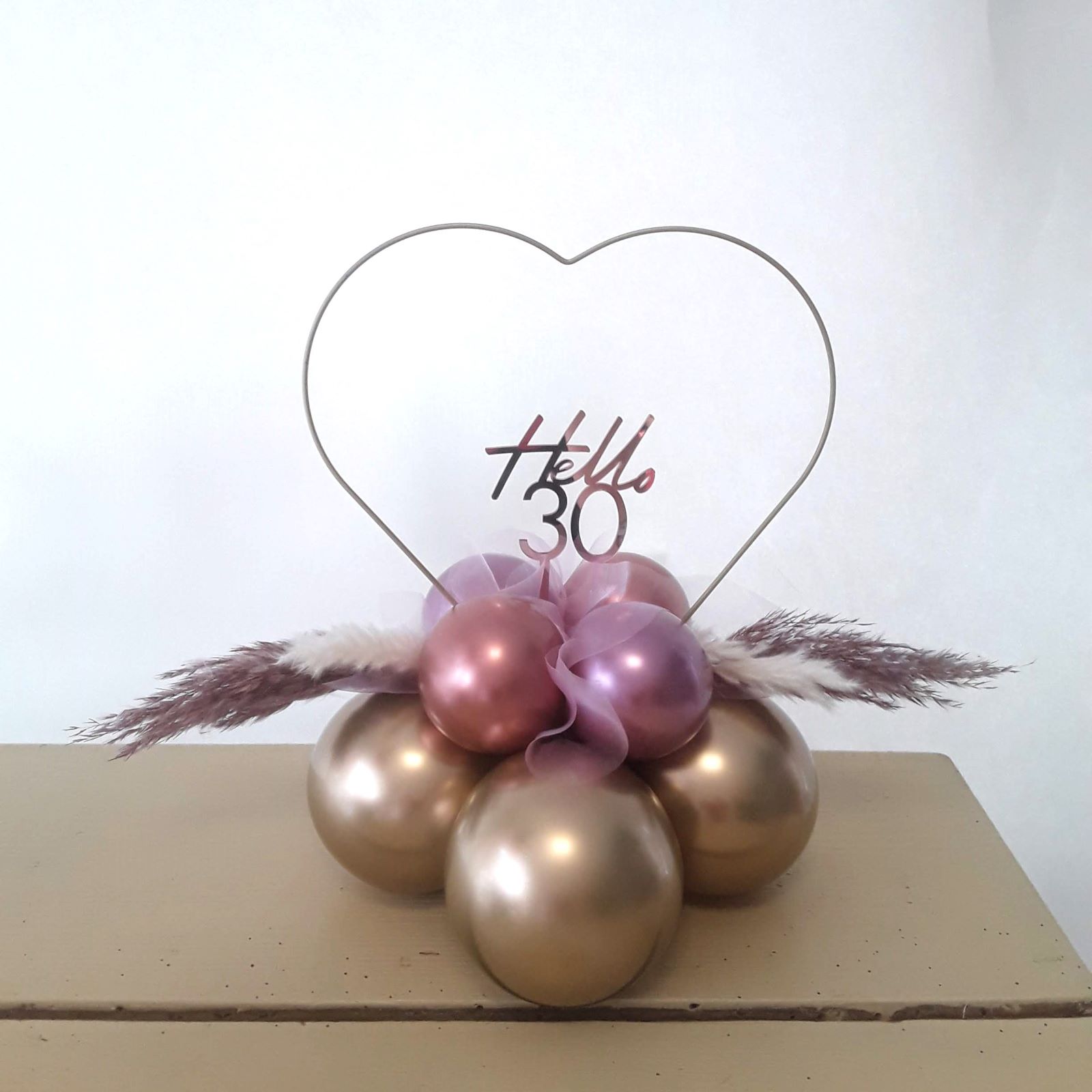 Roségoldener Ballon mit goldenem Schriftzug 'Hello 30' auf Herzständer, stilvoll arrangiert.