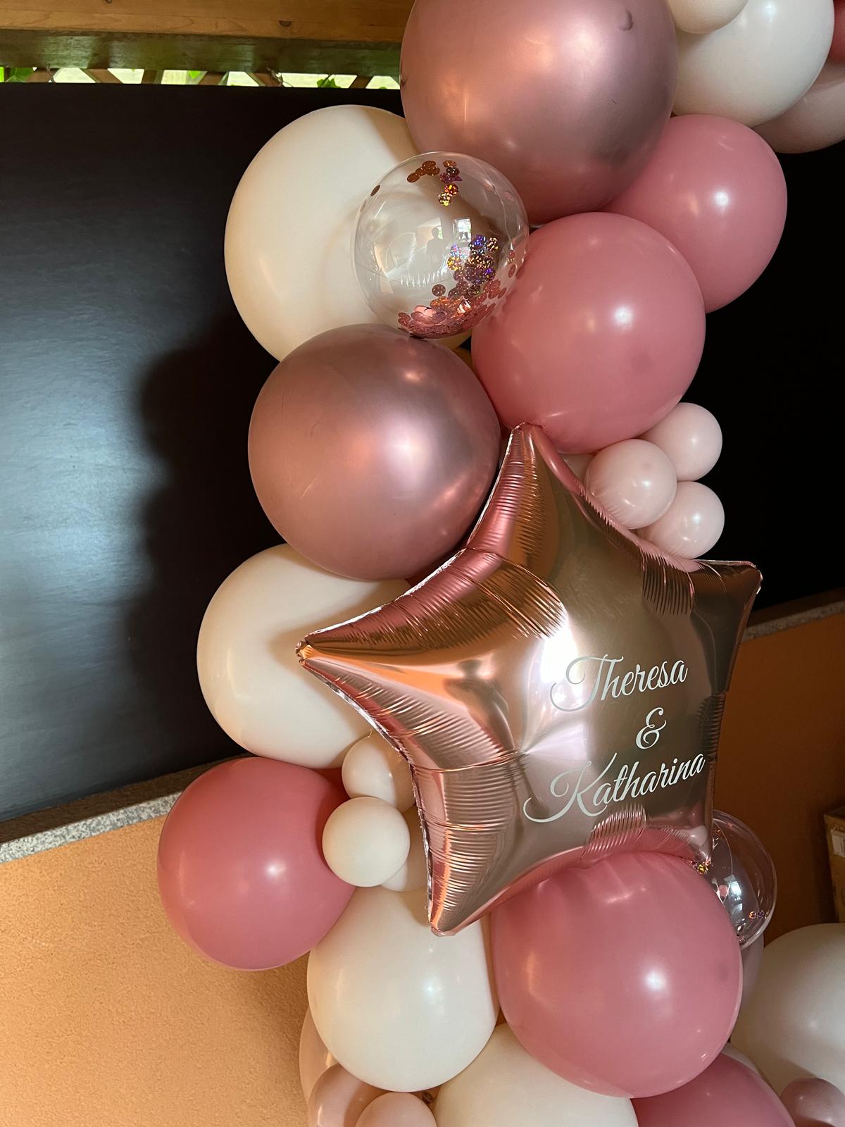 Ringbogen aus Ballons in Roségold, Rosa, Pink und Weiß, dekoriert mit großen Sternfolienballons mit Aufdruck 'Theresa&Katharina' und transparenten Konfettiballons
