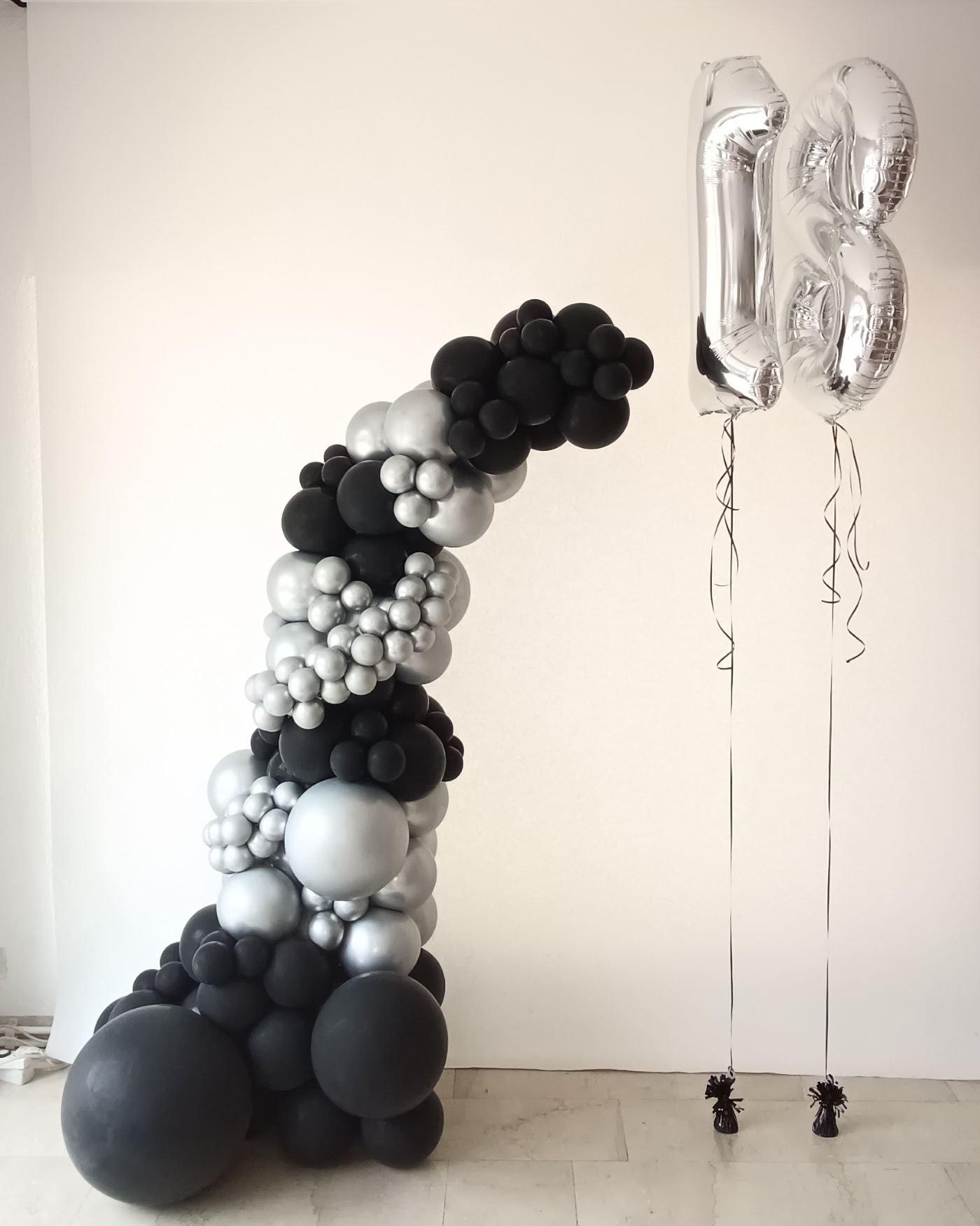 Ballon-Halbbogen in schwarz und silber, daneben 2 Folienballons mit den Nummern 1 und 8 in Silber an schwarzen Gewichten