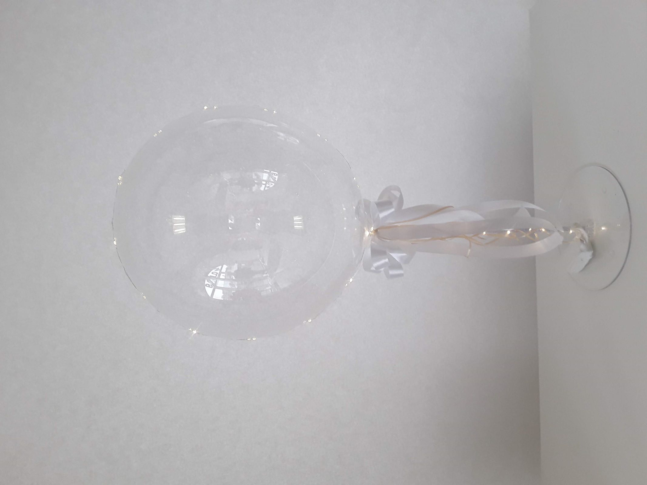 Transparenter Ballon auf Tischständer mit weißer Schleife und Lichterkette