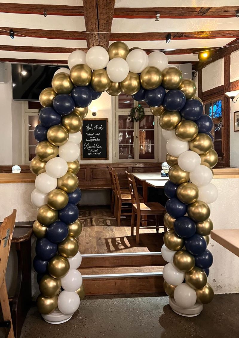 Rundbogen aus navyblauen, goldenen und weißen Ballons, symmetrisch aufgebaut in einem Eingangsbogen