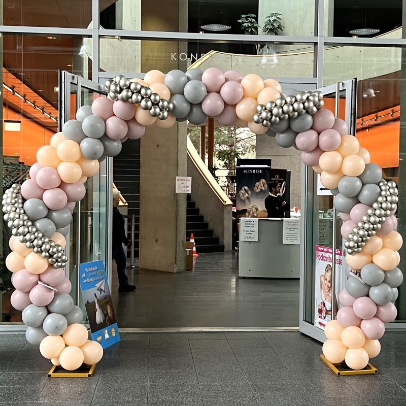 Rundbogen aus Ballons in Pastell und Silber, aufgebaut im Eingangsbereich einer Messehalle